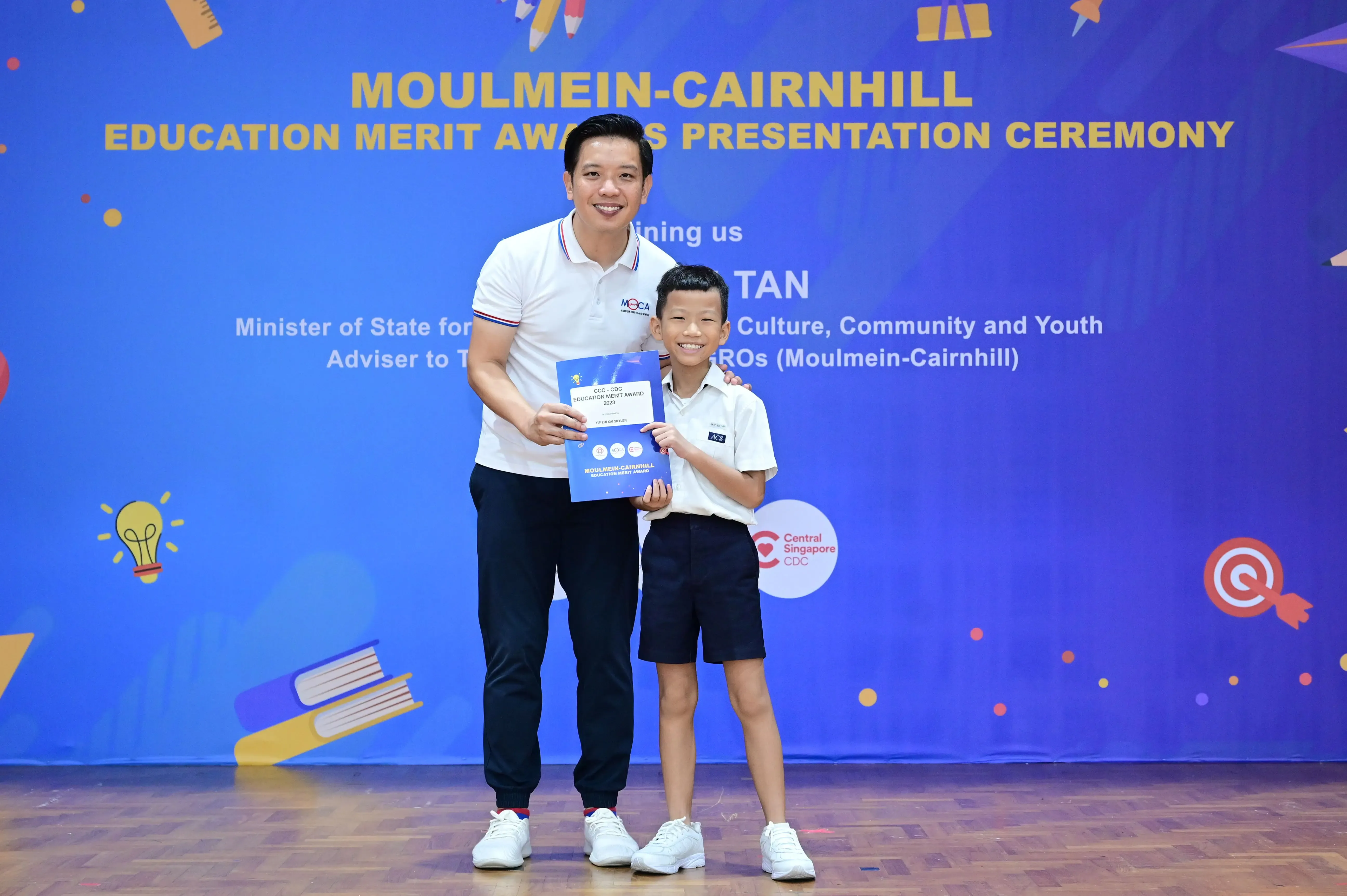 A man and a young boy hold an award certificate at the Moulmein-Cairnhill Education Merit Awards Presentation Ceremony.