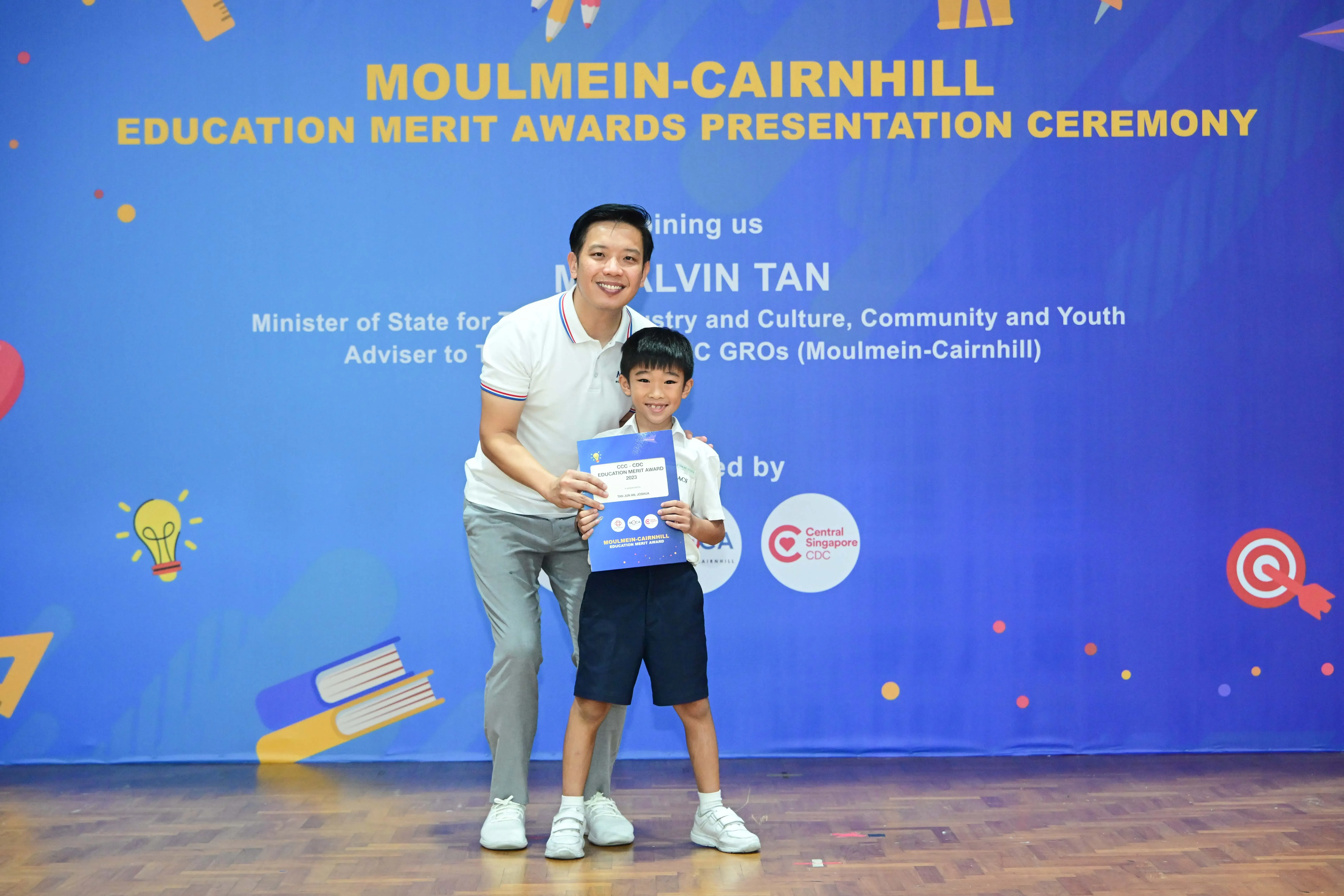 A man and a young boy pose together holding a certificate at the Moulmein-Cairnhill Education Merit Awards ceremony.