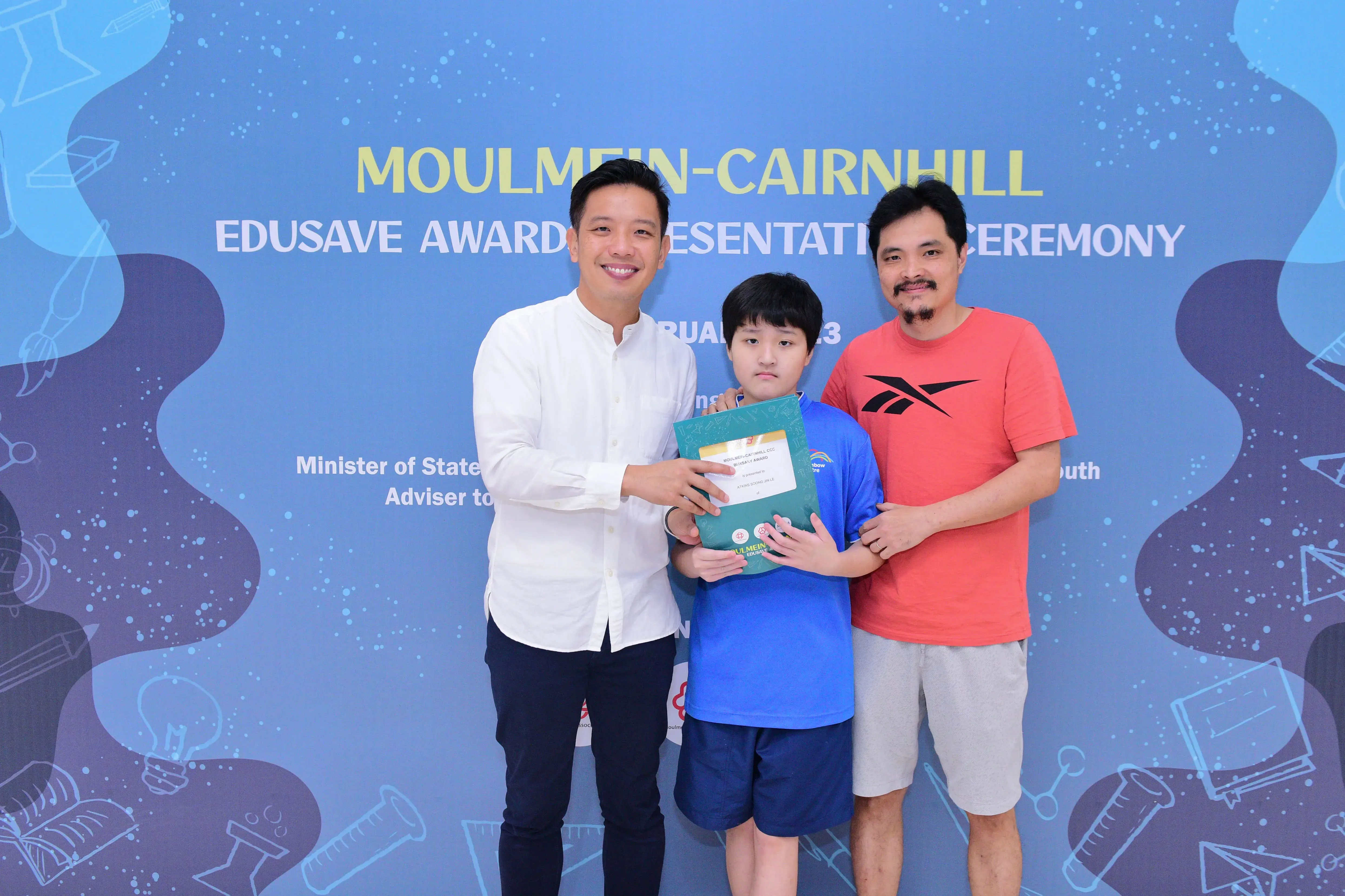 Two men and a boy pose with a certificate at the Moulmein-Cairnhill Edusave Awards Presentation Ceremony.