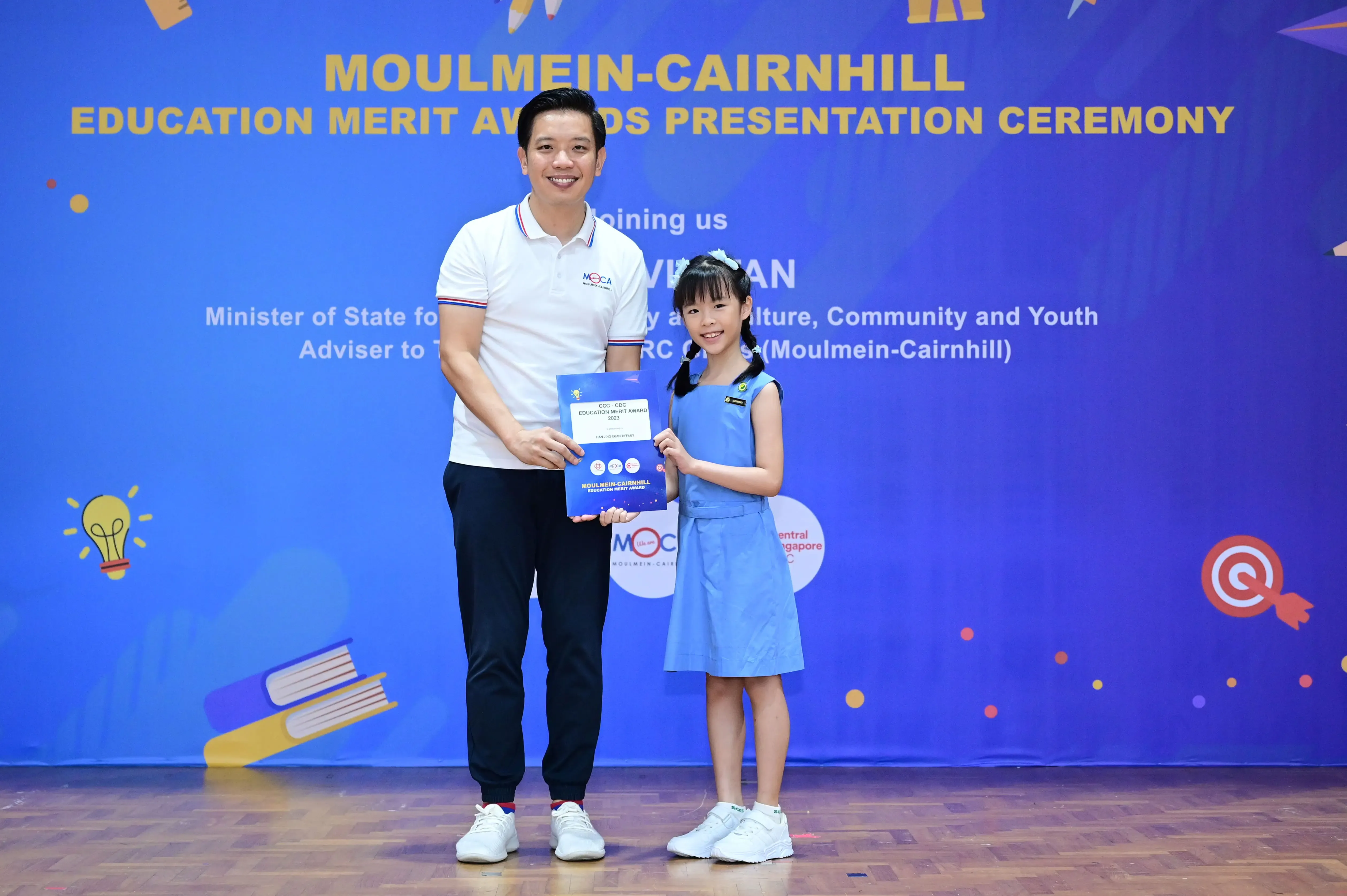 A man and a young girl hold an award certificate at the Moulmein-Cairnhill Education Merit Awards Presentation Ceremony.