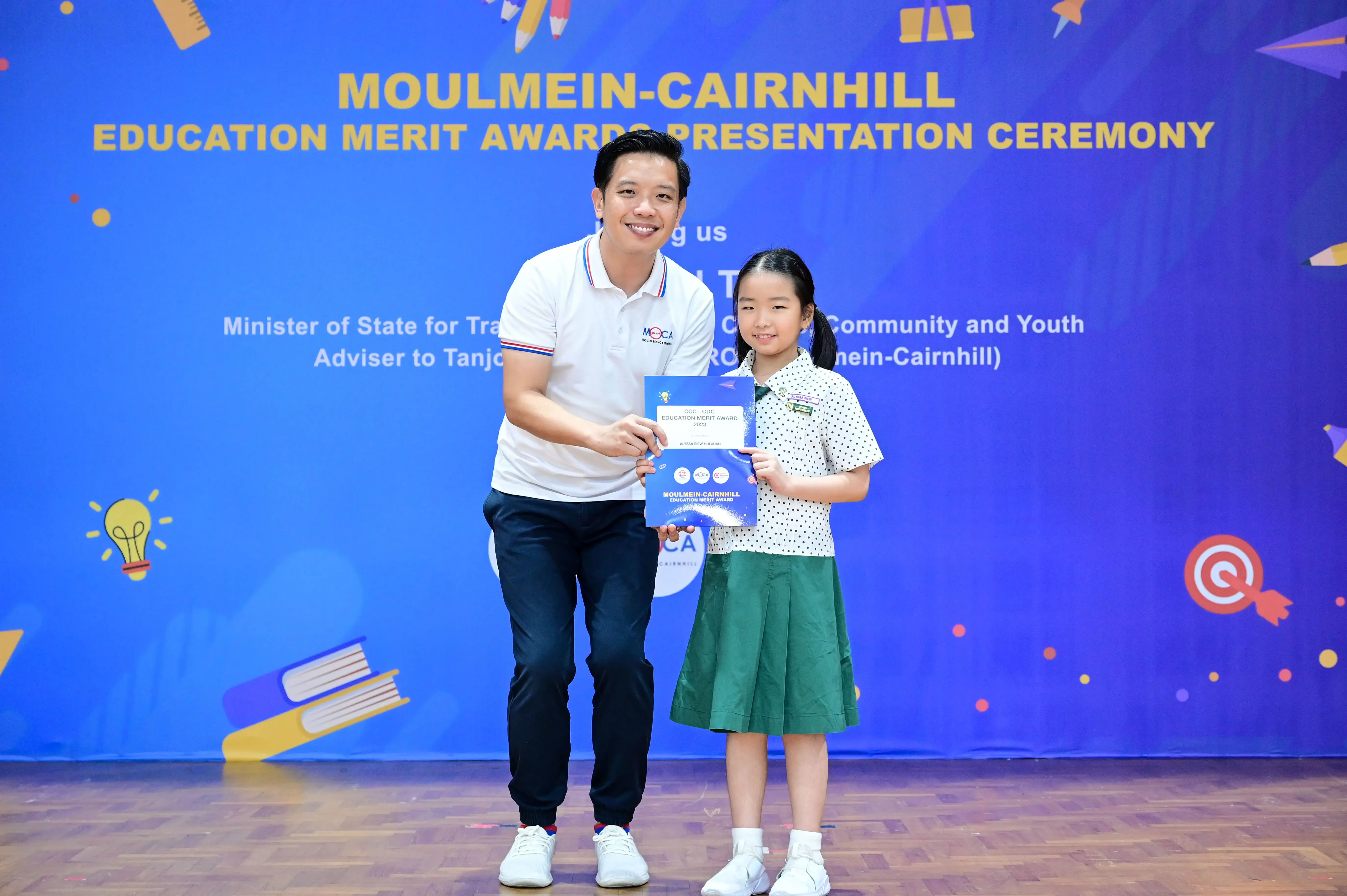 Man and young girl hold an award certificate at the Moulmein-Cairnhill Education Merit Awards Presentation Ceremony.