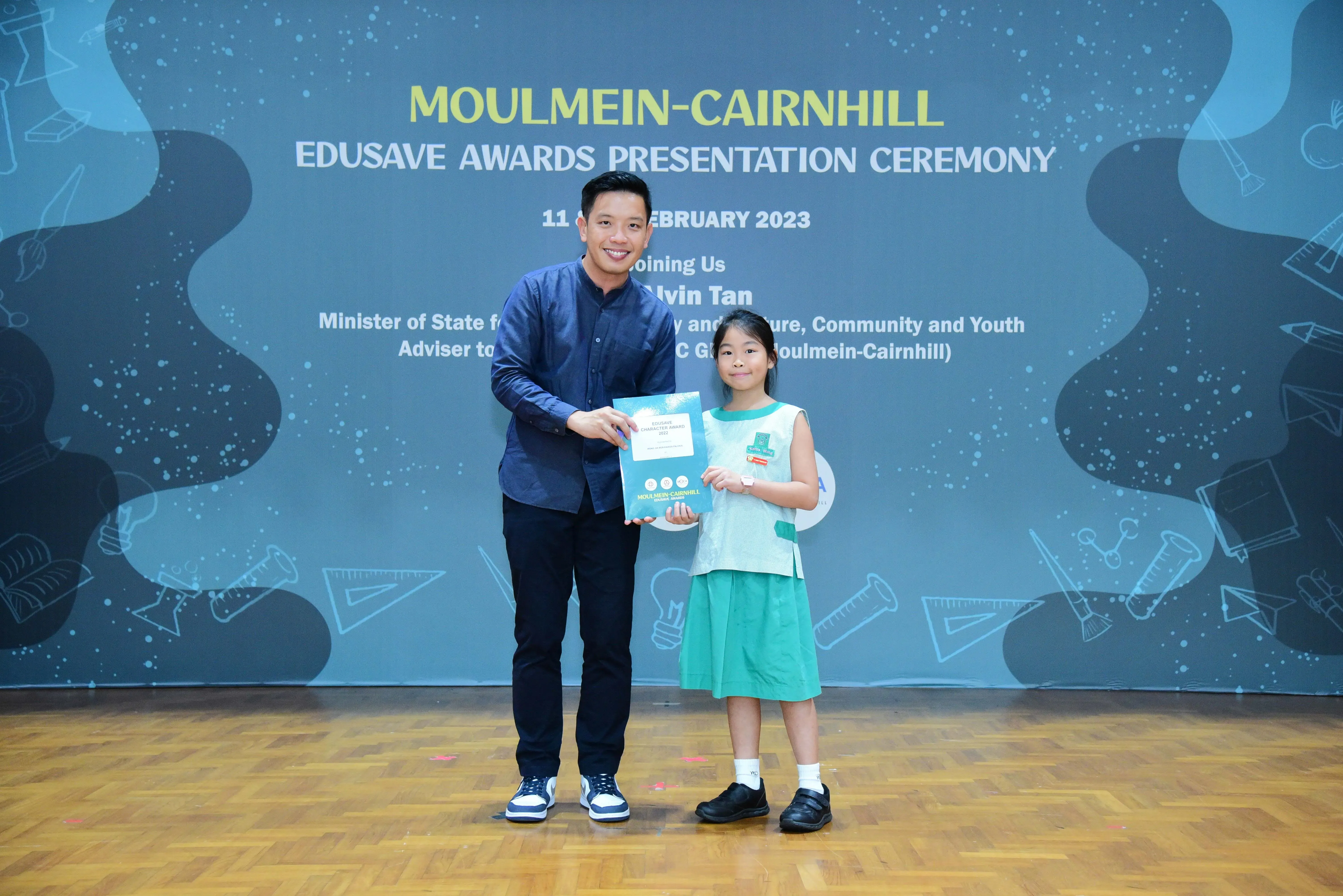 A man and a young girl hold an award certificate at the Moulmein-Cairnhill Edusave Awards Ceremony, February 2023.
