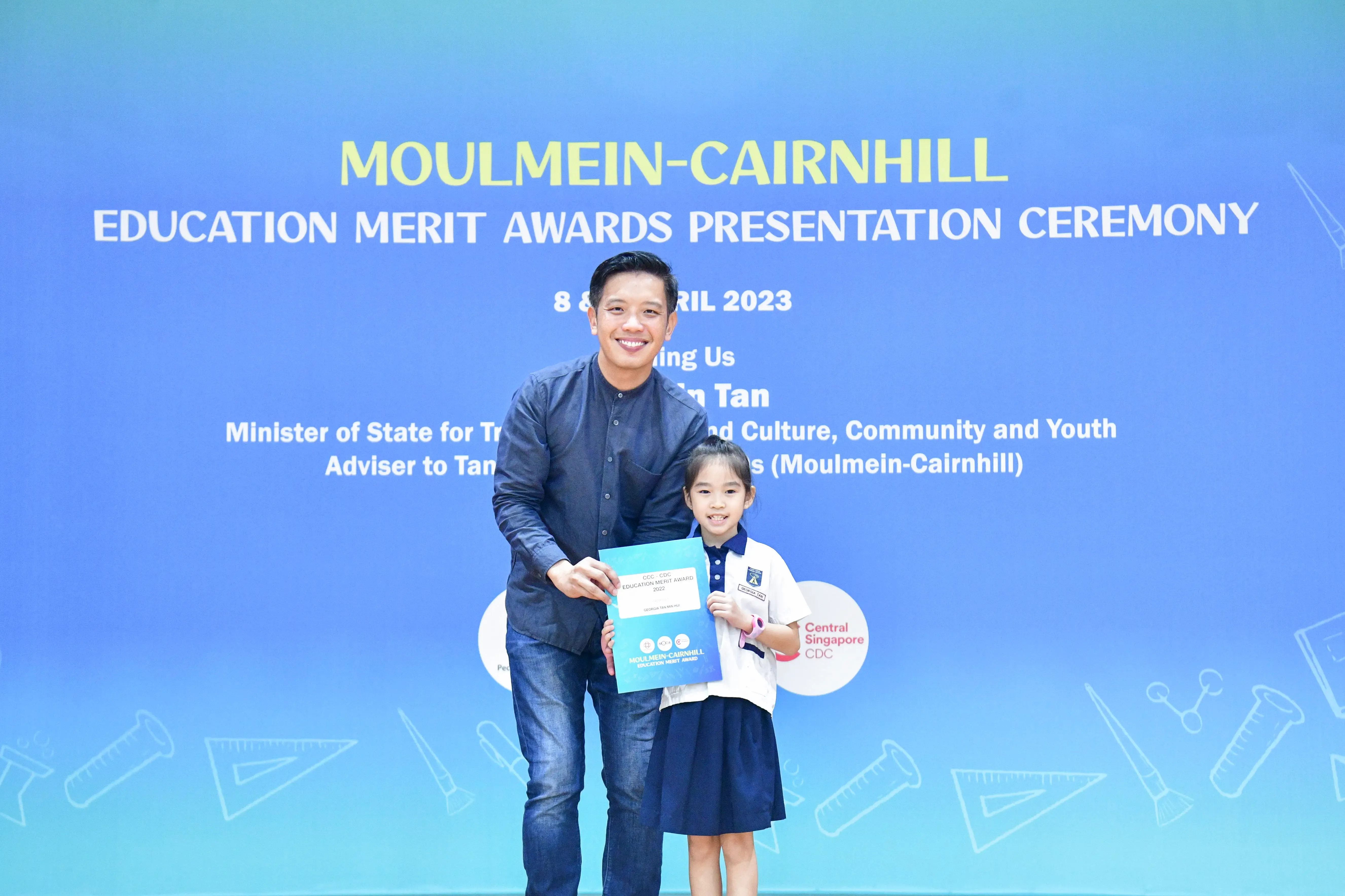 A man and a young girl in school uniform hold a certificate at the Moulmein-Cairnhill Education Merit Awards 2023.