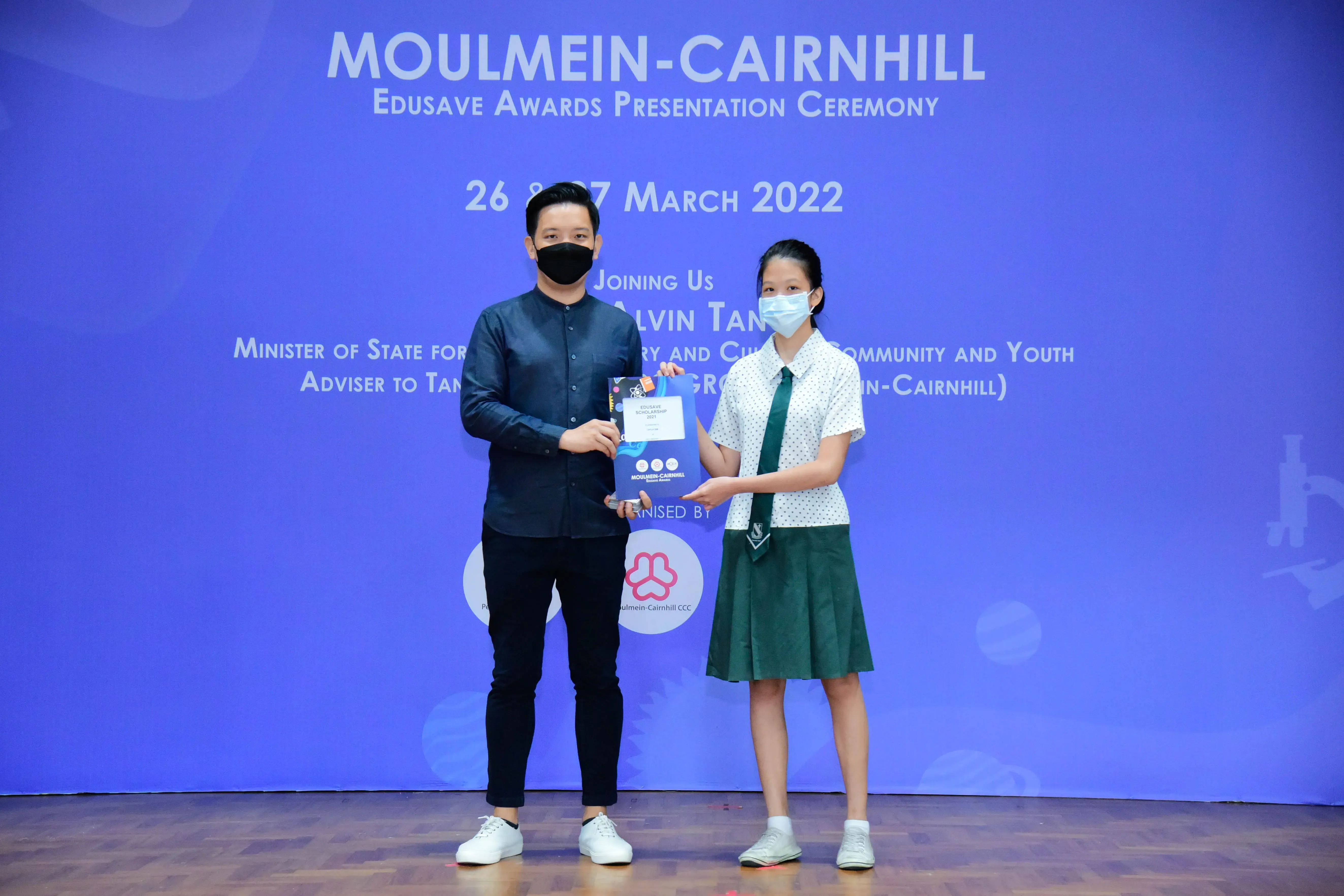 Two masked people hold a certificate at the Moulmein-Cairnhill Edusave Awards Ceremony, March 2022.