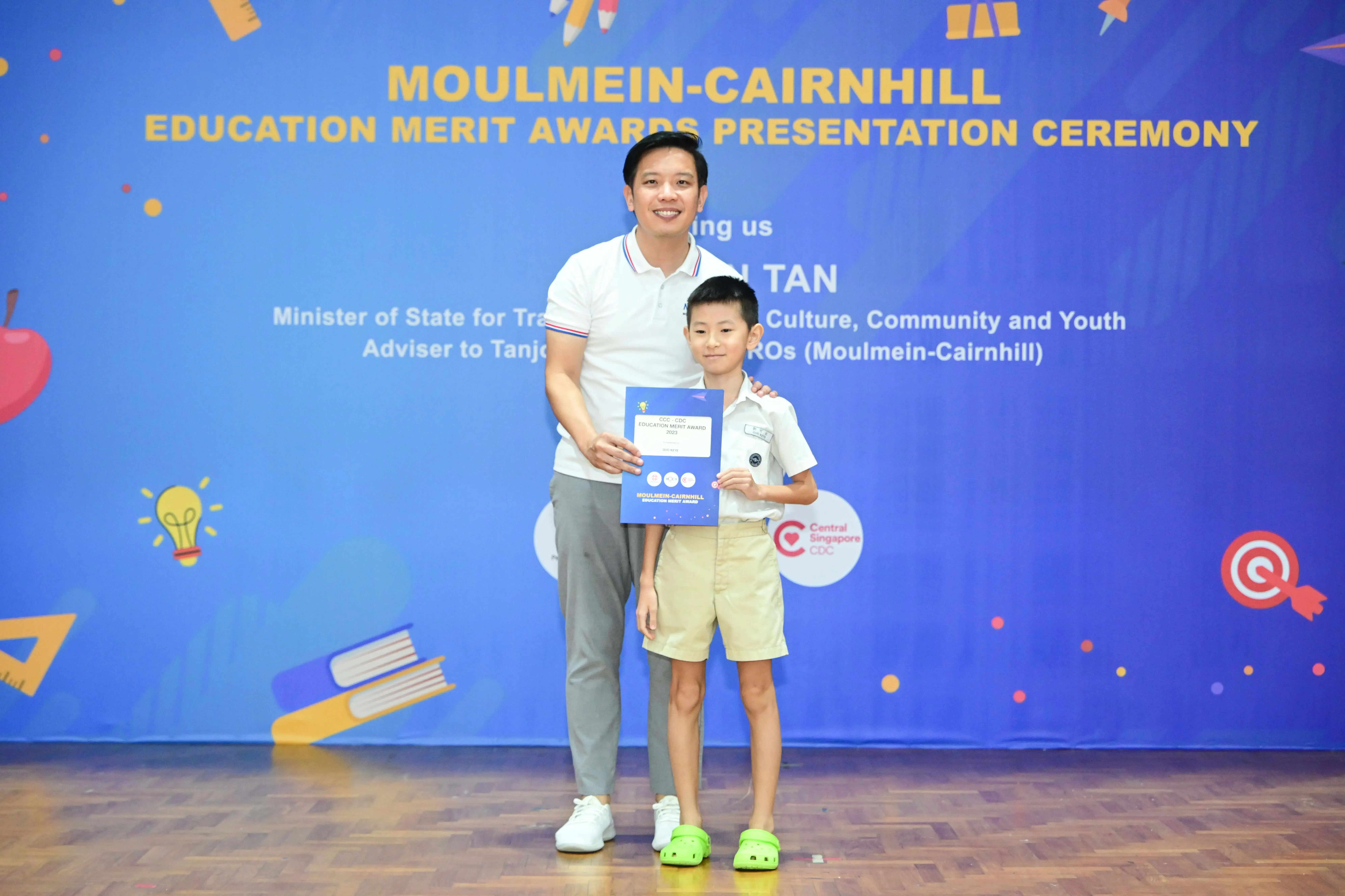 A man and a young boy holding a certificate at the Moulmein-Cairnhill Education Merit Awards Presentation Ceremony.
