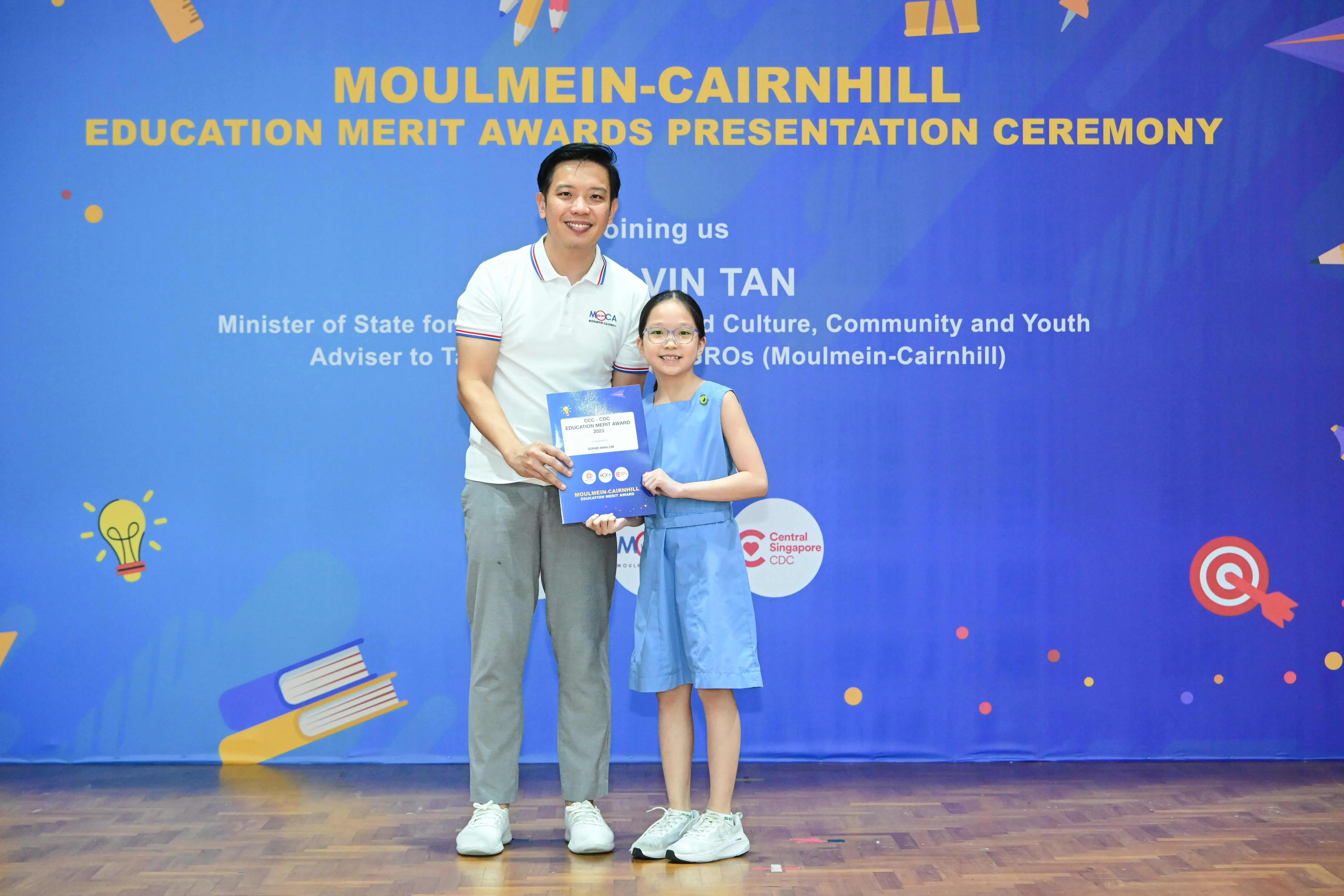A man and a young girl holding an award certificate pose at the Moulmein-Cairnhill Education Merit Awards Ceremony.