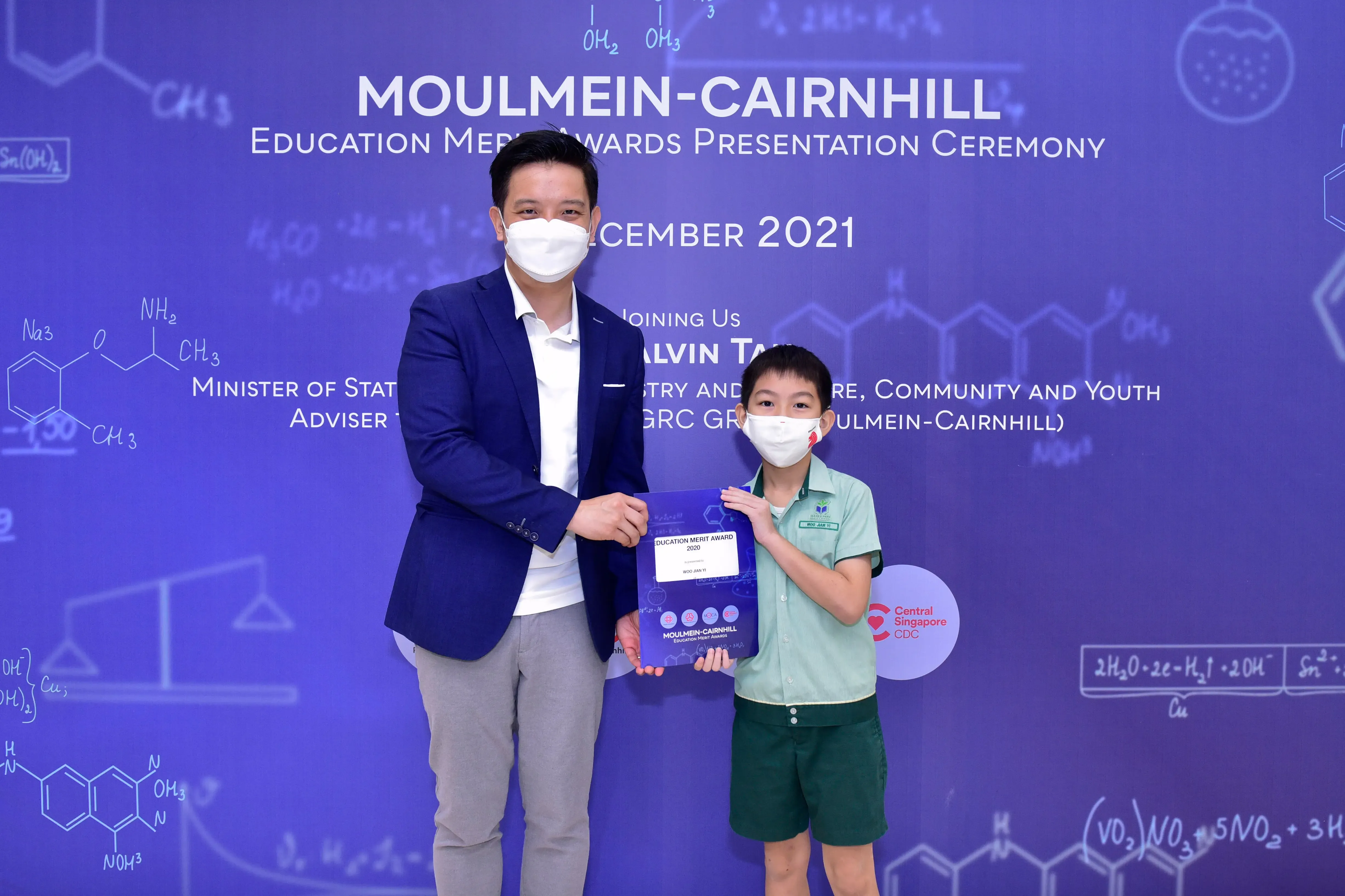 An adult and a young student wearing masks hold an award plaque at the Moulmein-Cairnhill Education Merit Awards 2021.