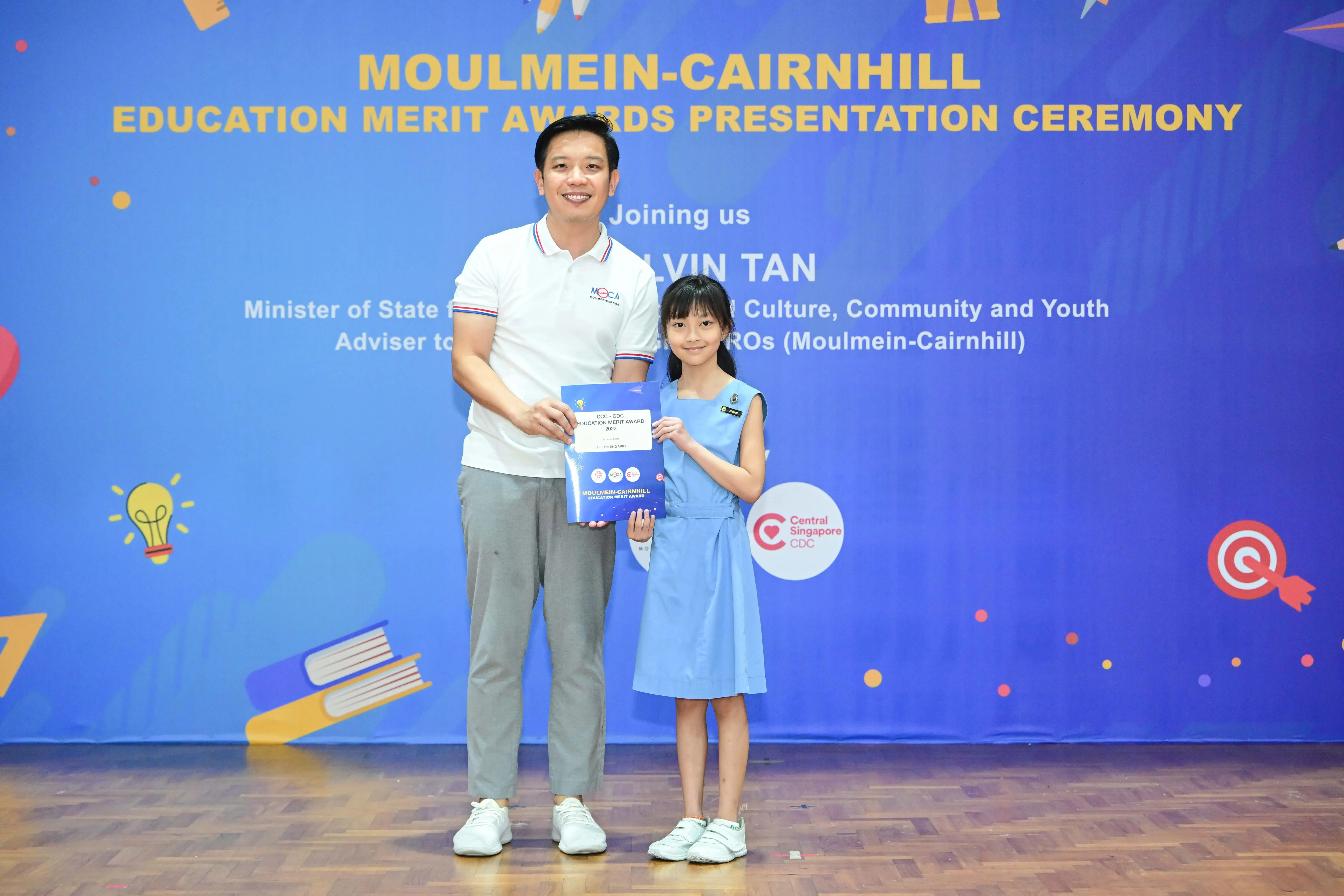 A man and a young girl hold a certificate at the Moulmein-Cairnhill Education Merit Awards Presentation Ceremony.