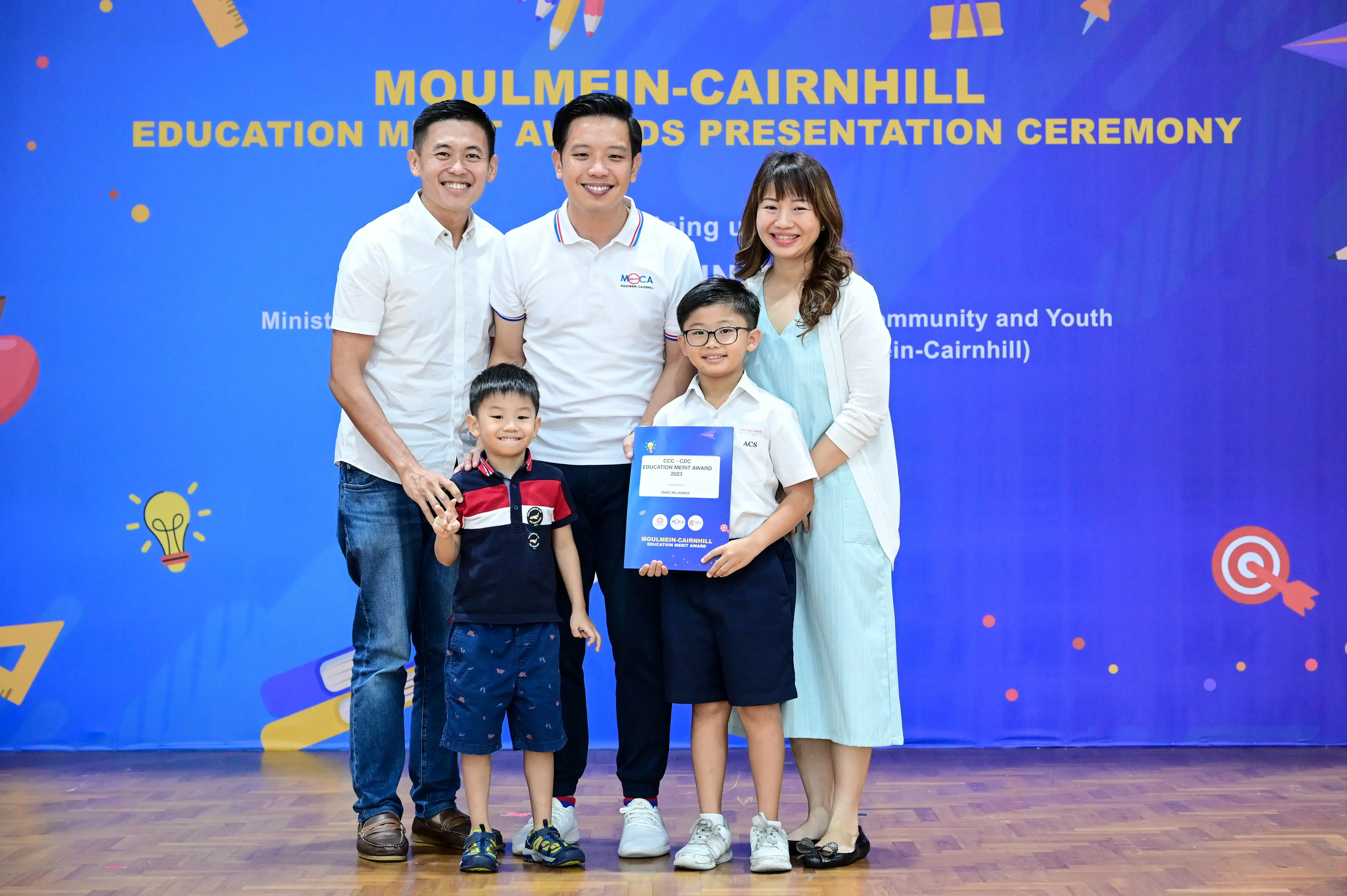 Five people pose smiling at the Moulmein-Cairnhill Education Merit Awards Presentation Ceremony, boy holding a certificate.