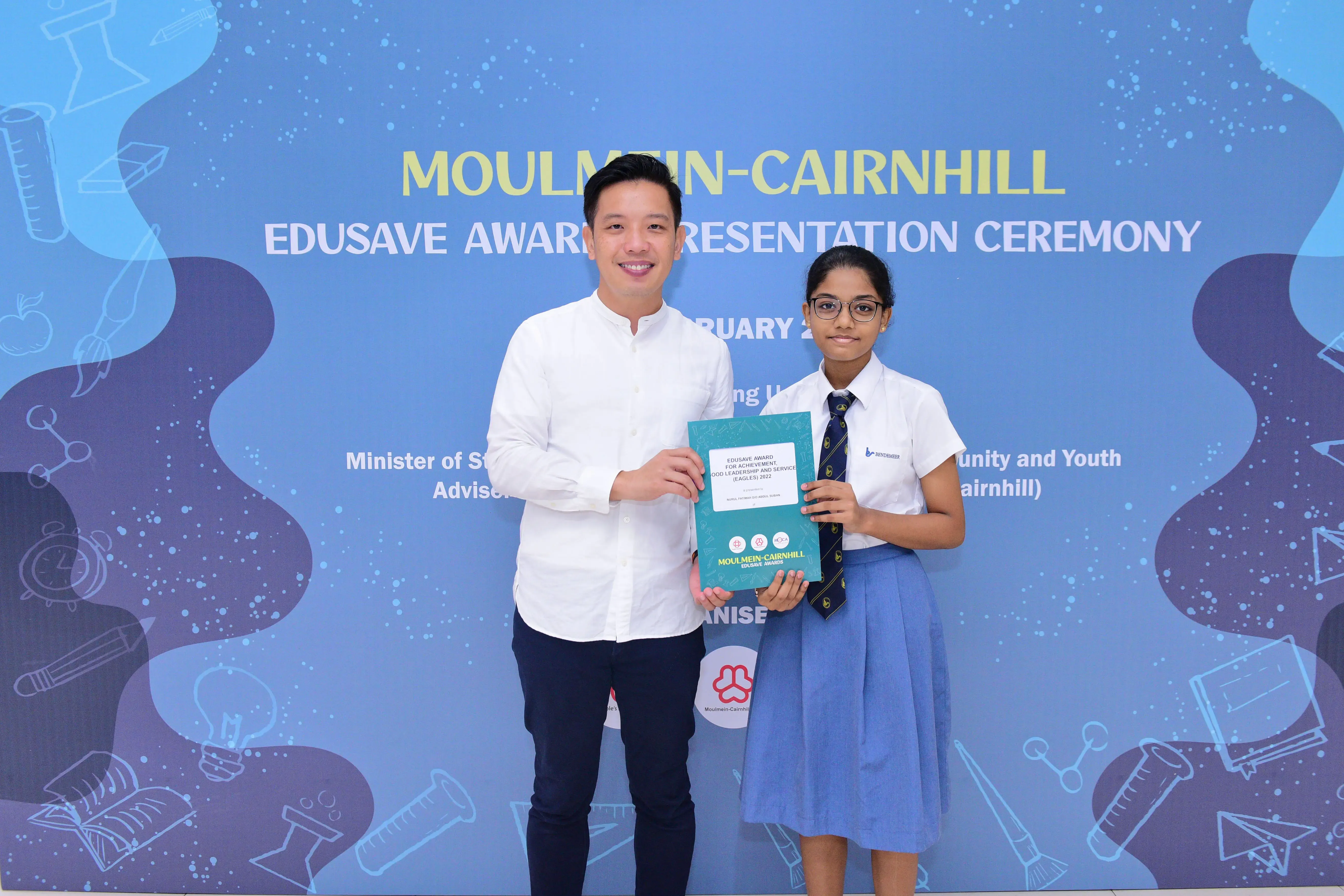 A man and a schoolgirl hold a teal certificate together at the Moulmein-Cairnhill Edusave Award Presentation Ceremony.