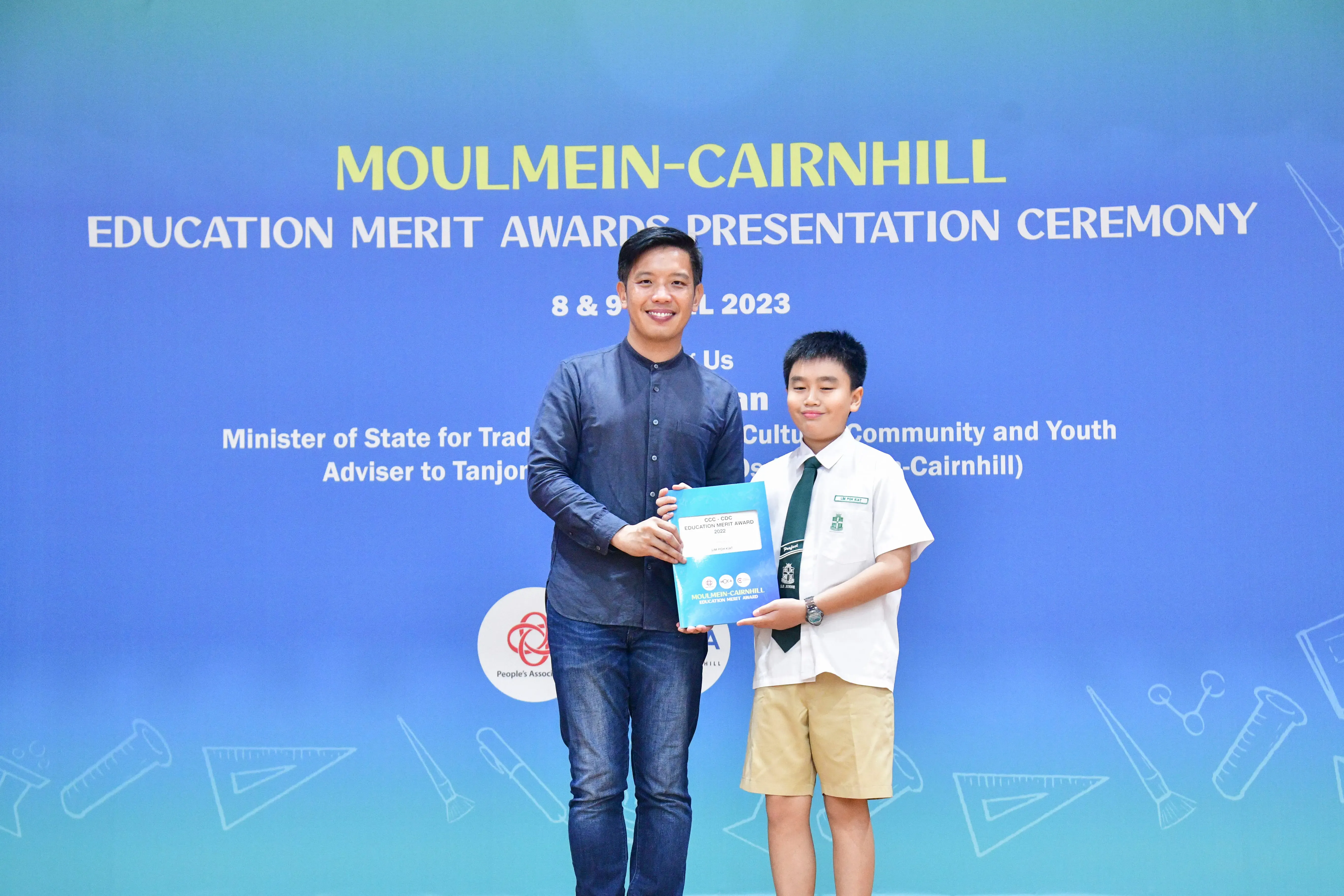 An adult and a uniformed student hold an award certificate at the Moulmein-Cairnhill Education Merit Awards Ceremony 2023.