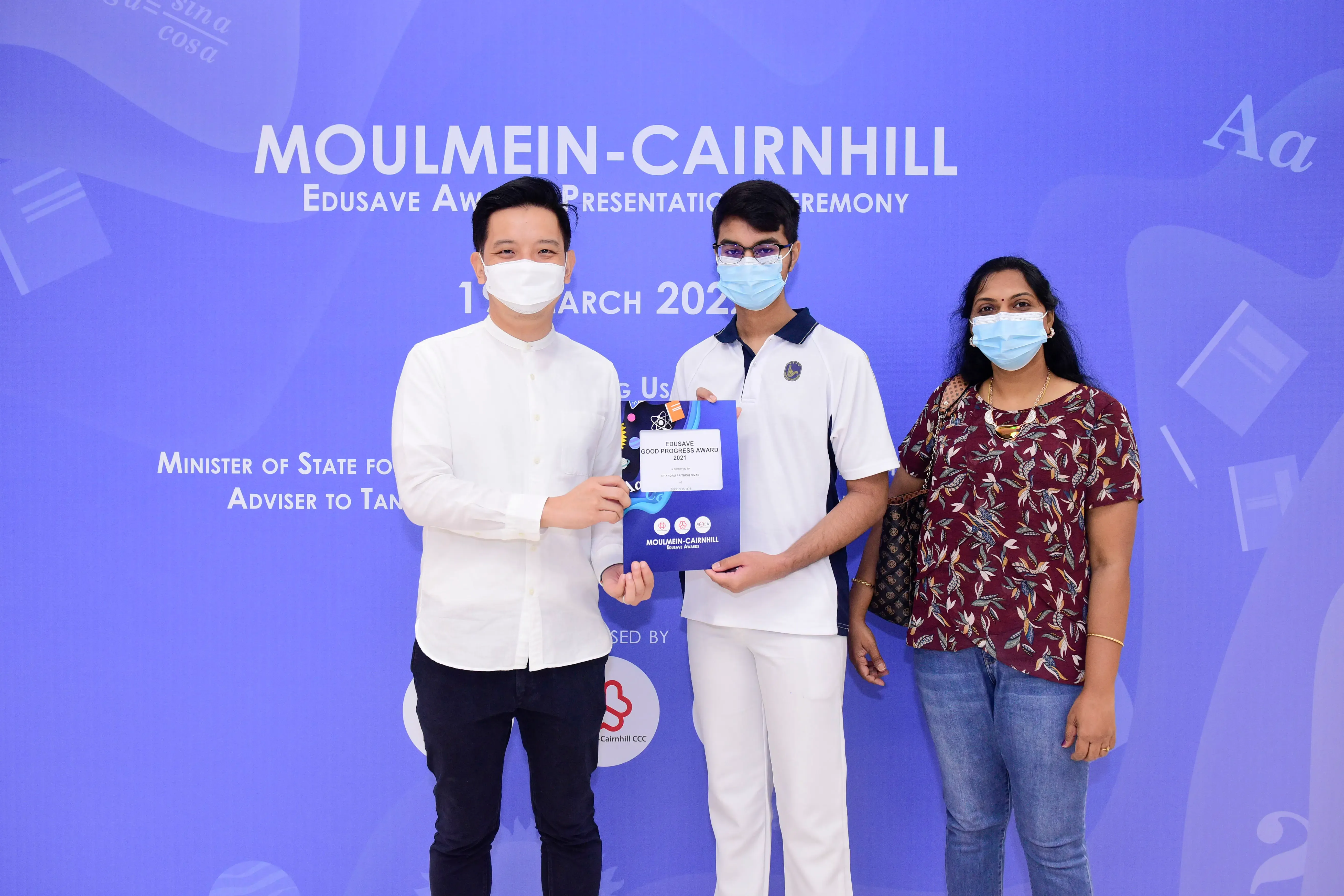 Three masked people pose at the Moulmein-Cairnhill Edusave Award Presentation Ceremony, holding an award certificate.