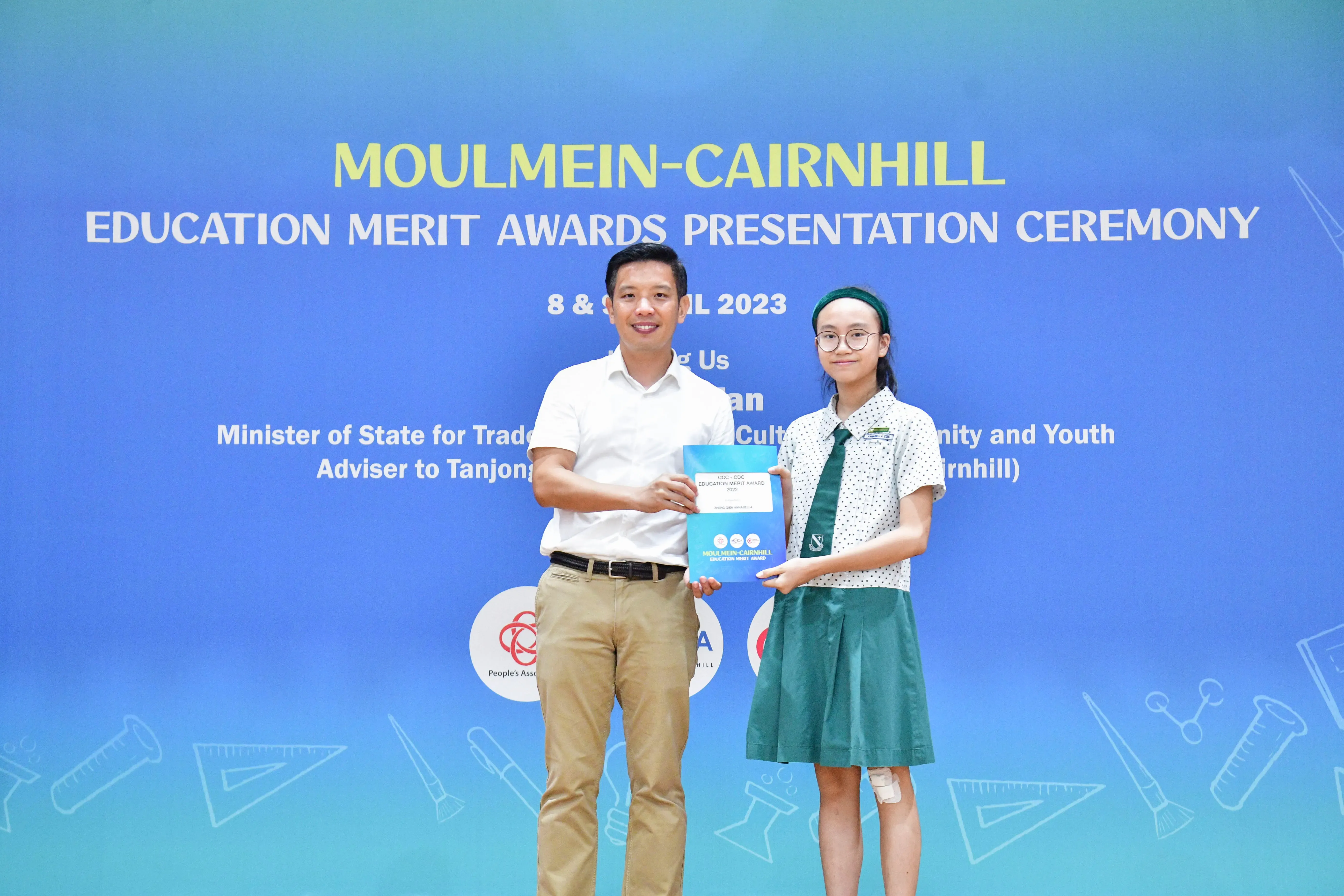 A man and a young girl in school uniform hold an award folder at the Moulmein-Cairnhill Education Merit Awards 2023.