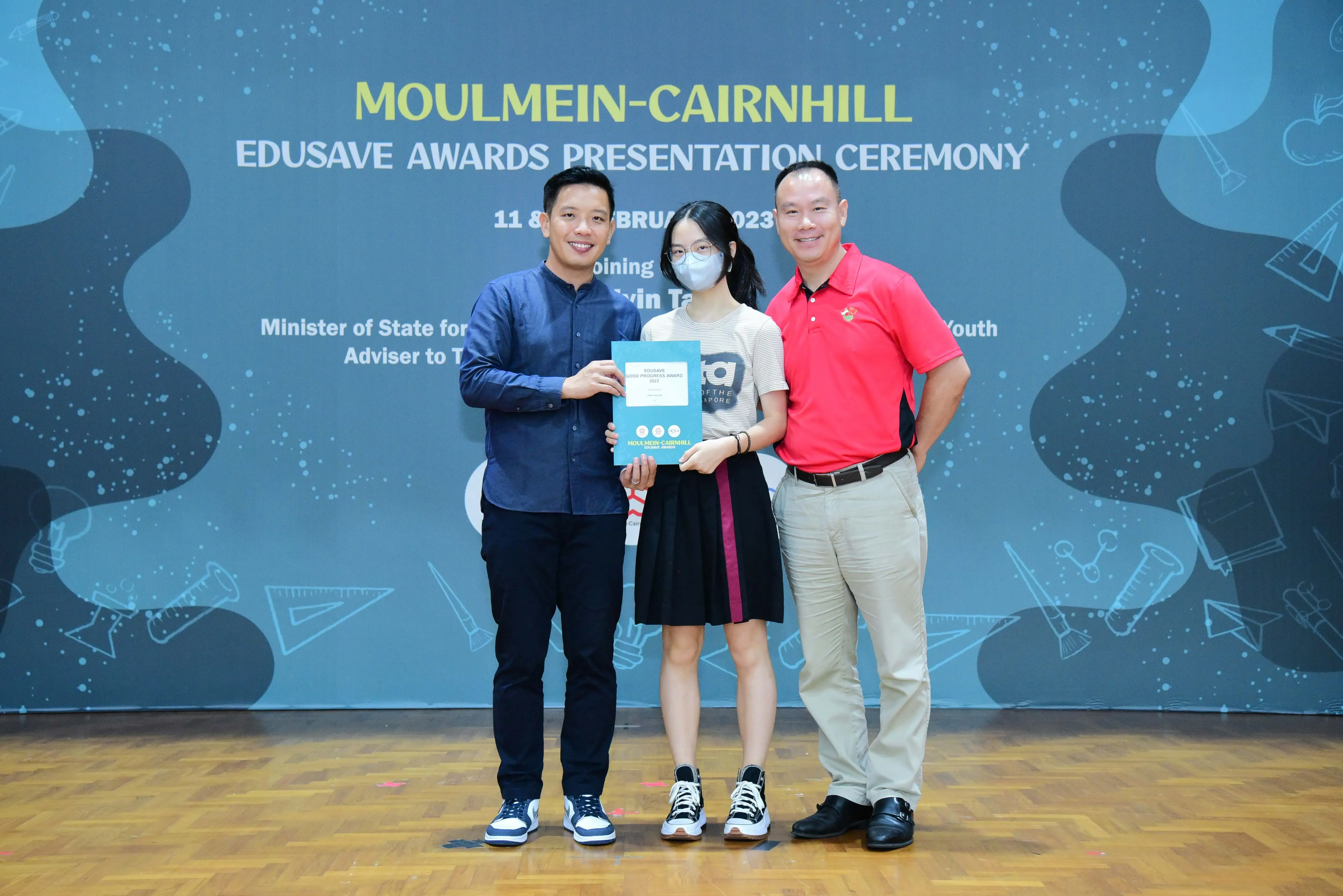 Three people pose holding a certificate at the Moulmein-Cairnhill Edusave Awards Presentation Ceremony 2023.