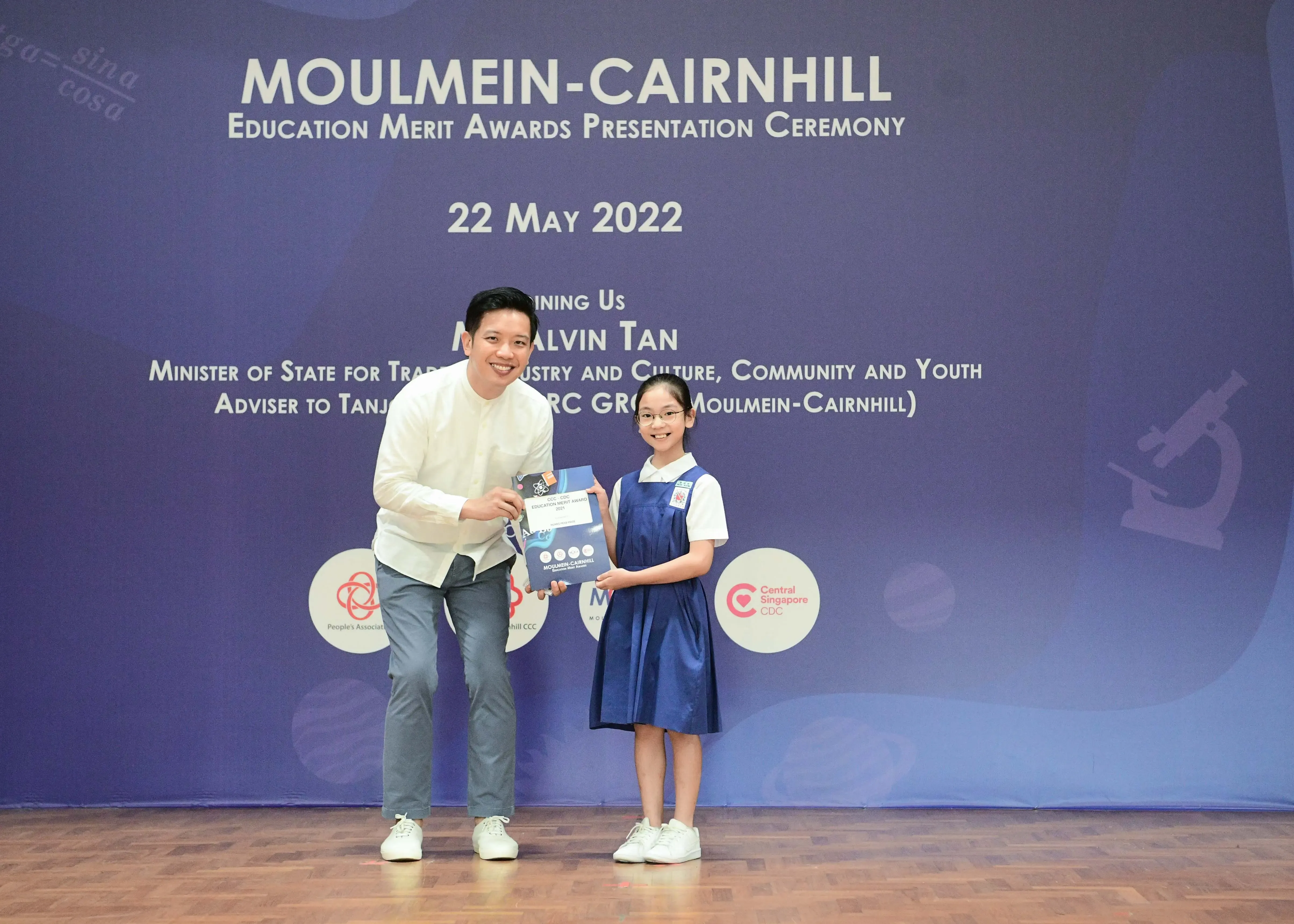 A man and a young girl in school uniform hold an award at the Moulmein-Cairnhill Education Merit Awards Ceremony, 22 May 2022.