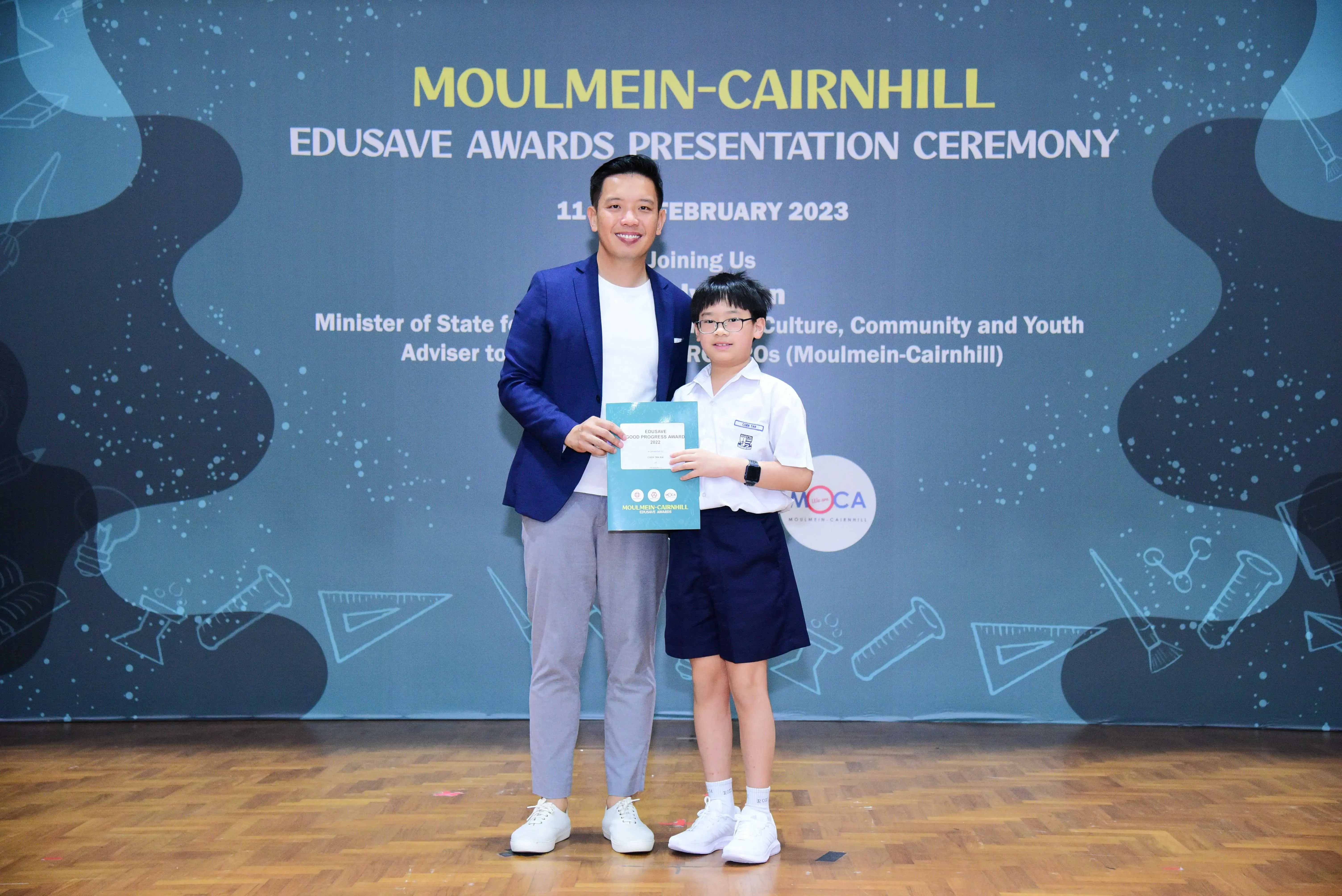 An adult and a young student holding a certificate at the Moulmein-Cairnhill Edusave Awards Ceremony, February 2023.