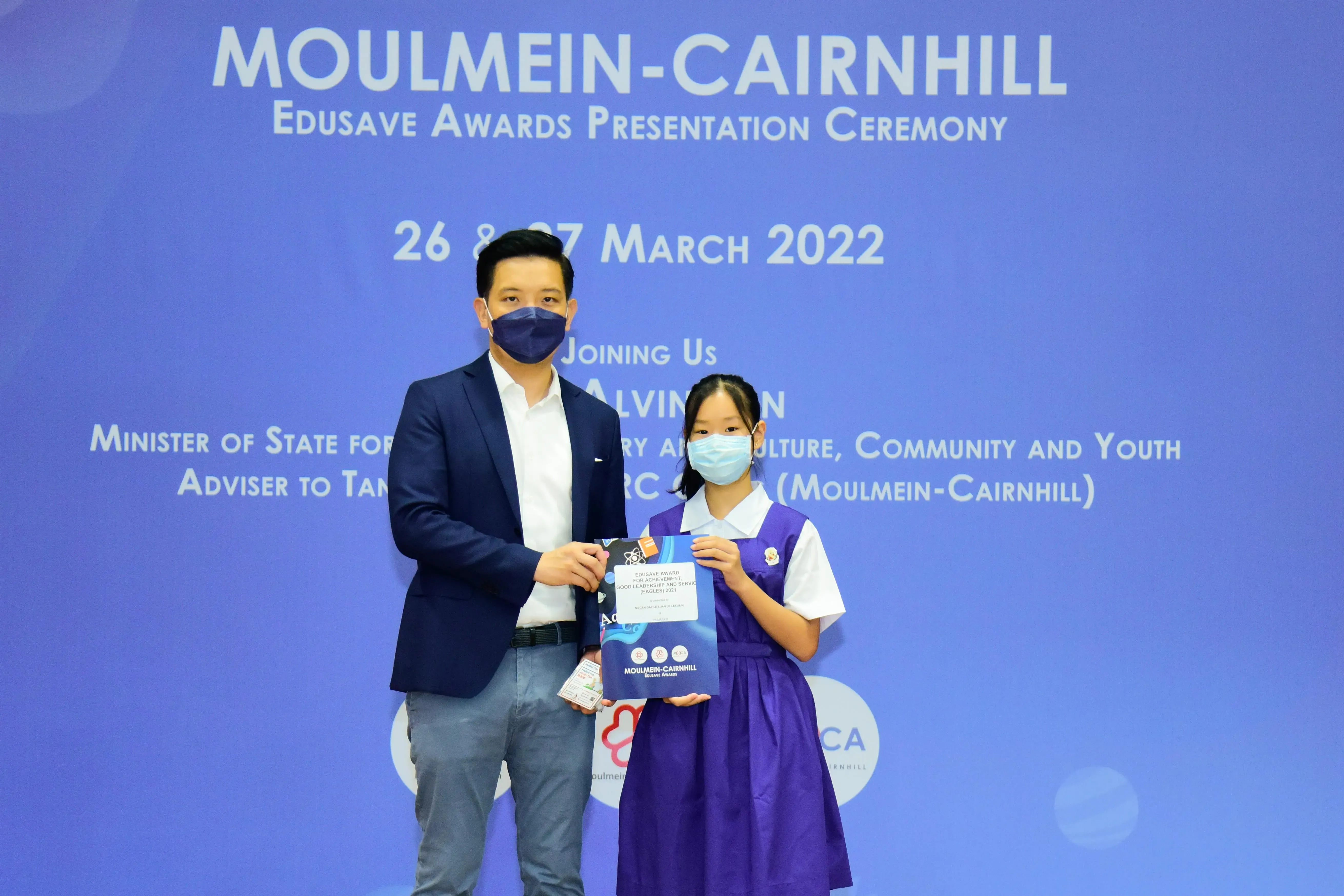 A man and a young girl in school uniform hold an award folder at the Moulmein-Cairnhill Edusave Awards Ceremony 2022.