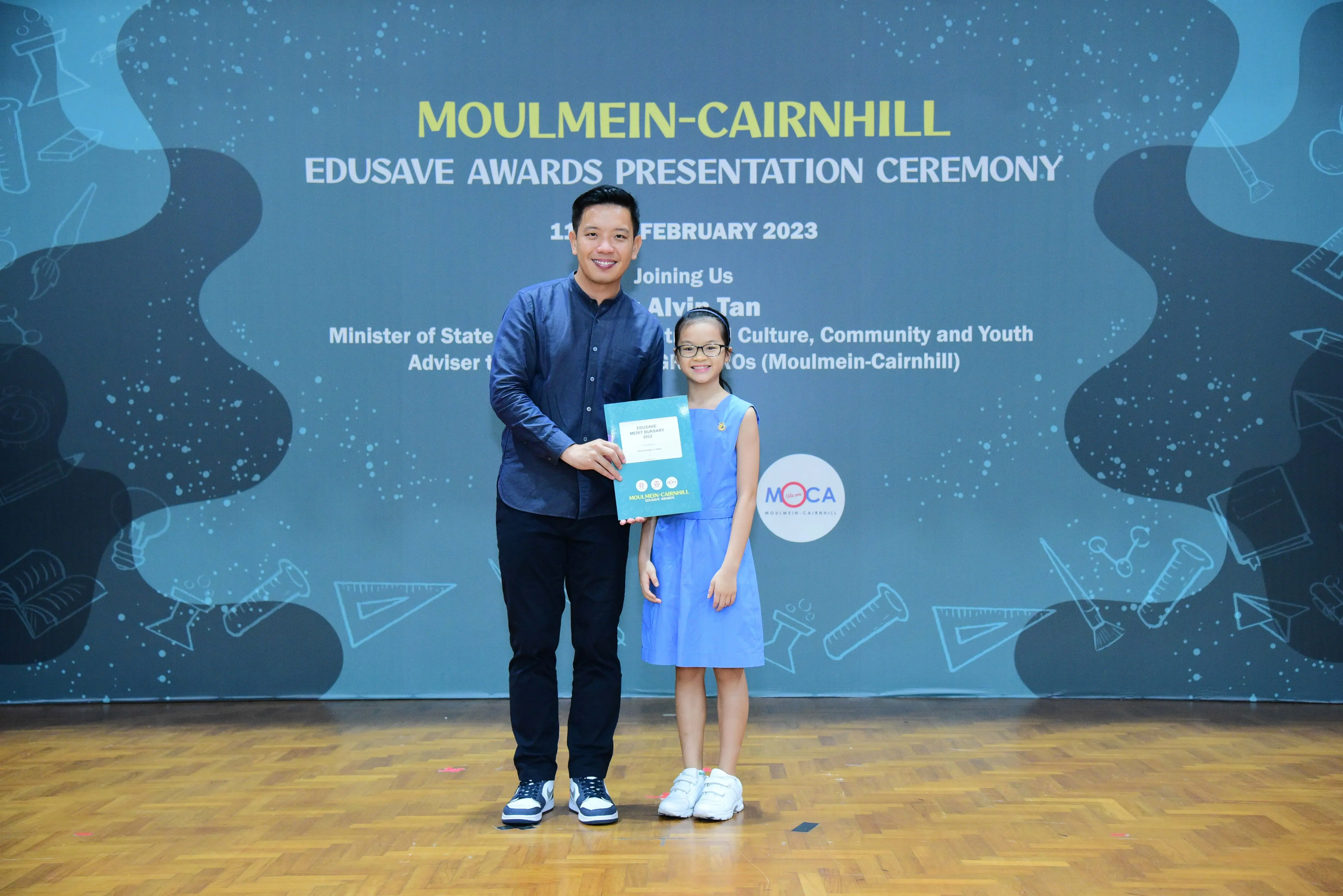 A man and a young girl hold a certificate at the Moulmein-Cairnhill Edusave Awards Presentation Ceremony, February 2023.