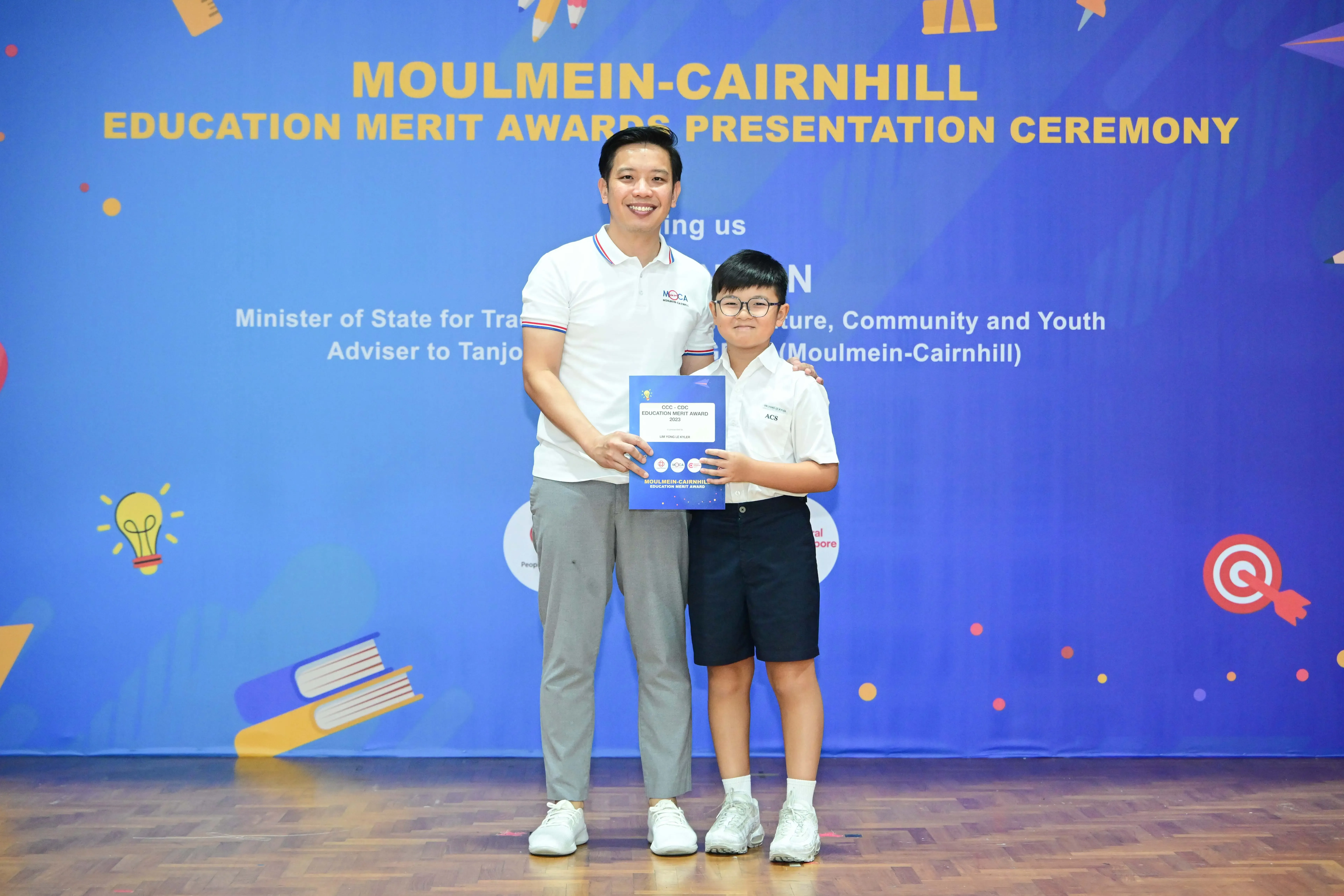 A man and a young boy hold an award certificate at the Moulmein-Cairnhill Education Merit Awards Presentation Ceremony.