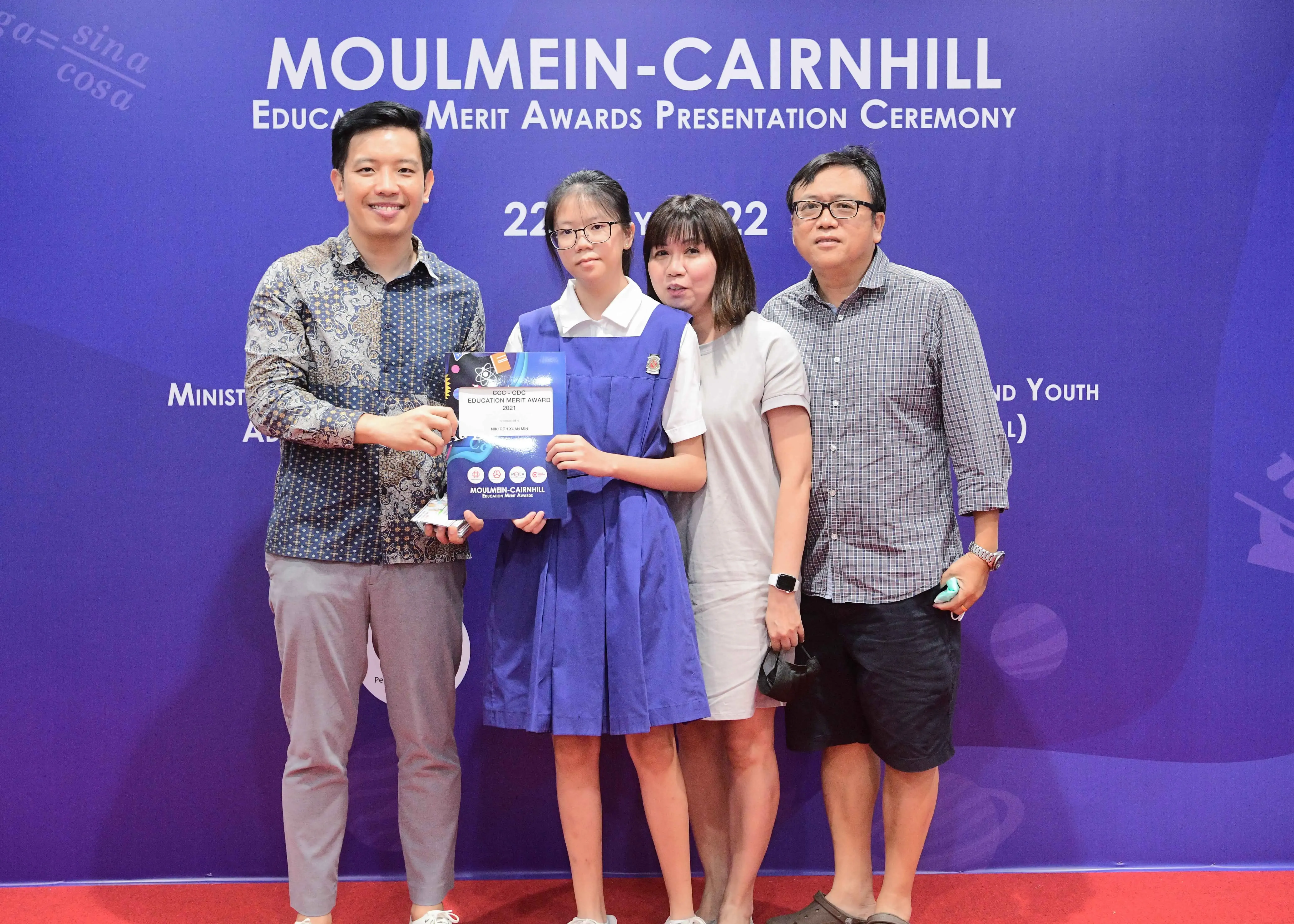 Four people pose at the Moulmein-Cairnhill Education Merit Awards Presentation Ceremony, student holding an award certificate.