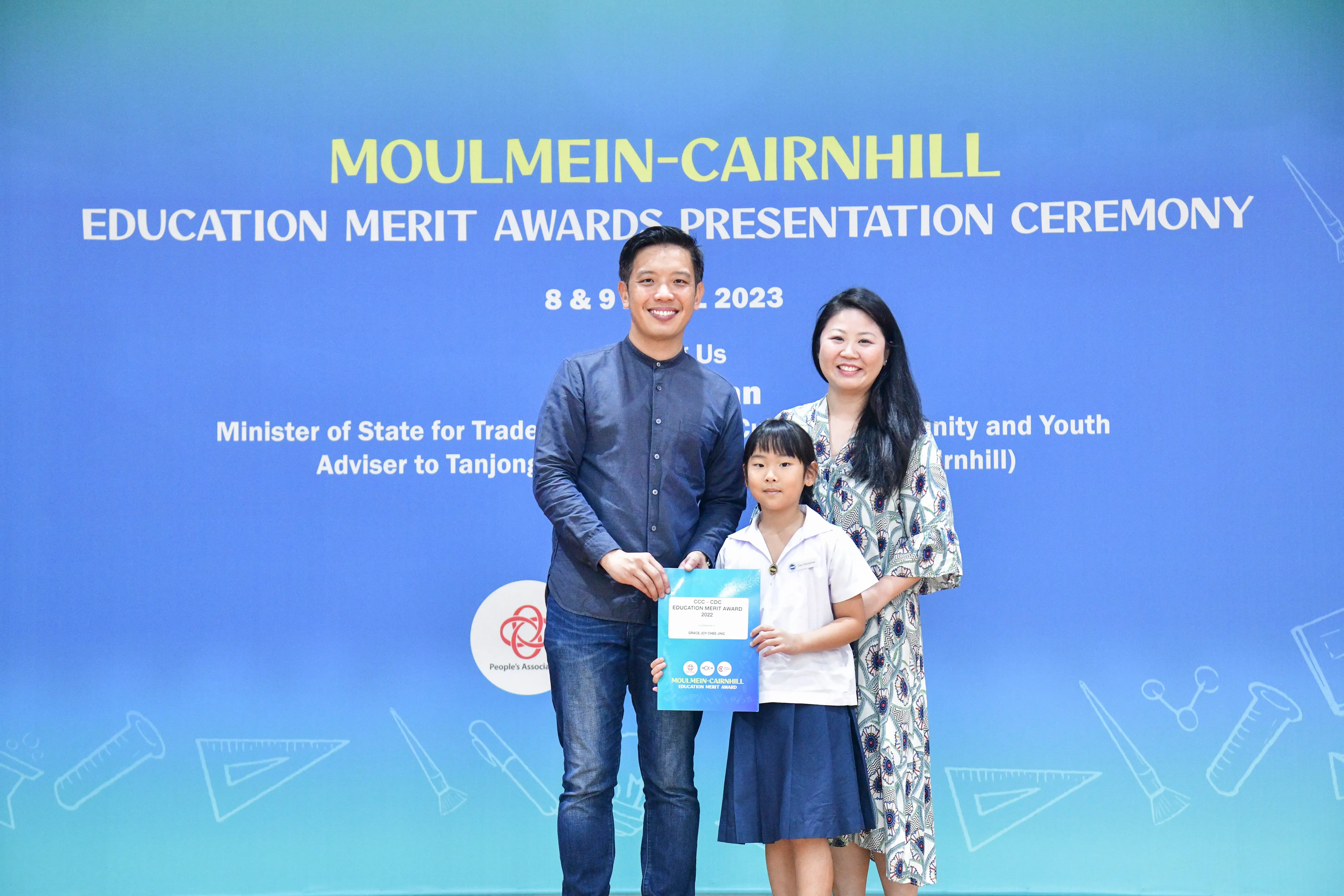 Two adults and a young girl hold an award certificate at the Moulmein-Cairnhill Education Merit Awards Ceremony 2023.