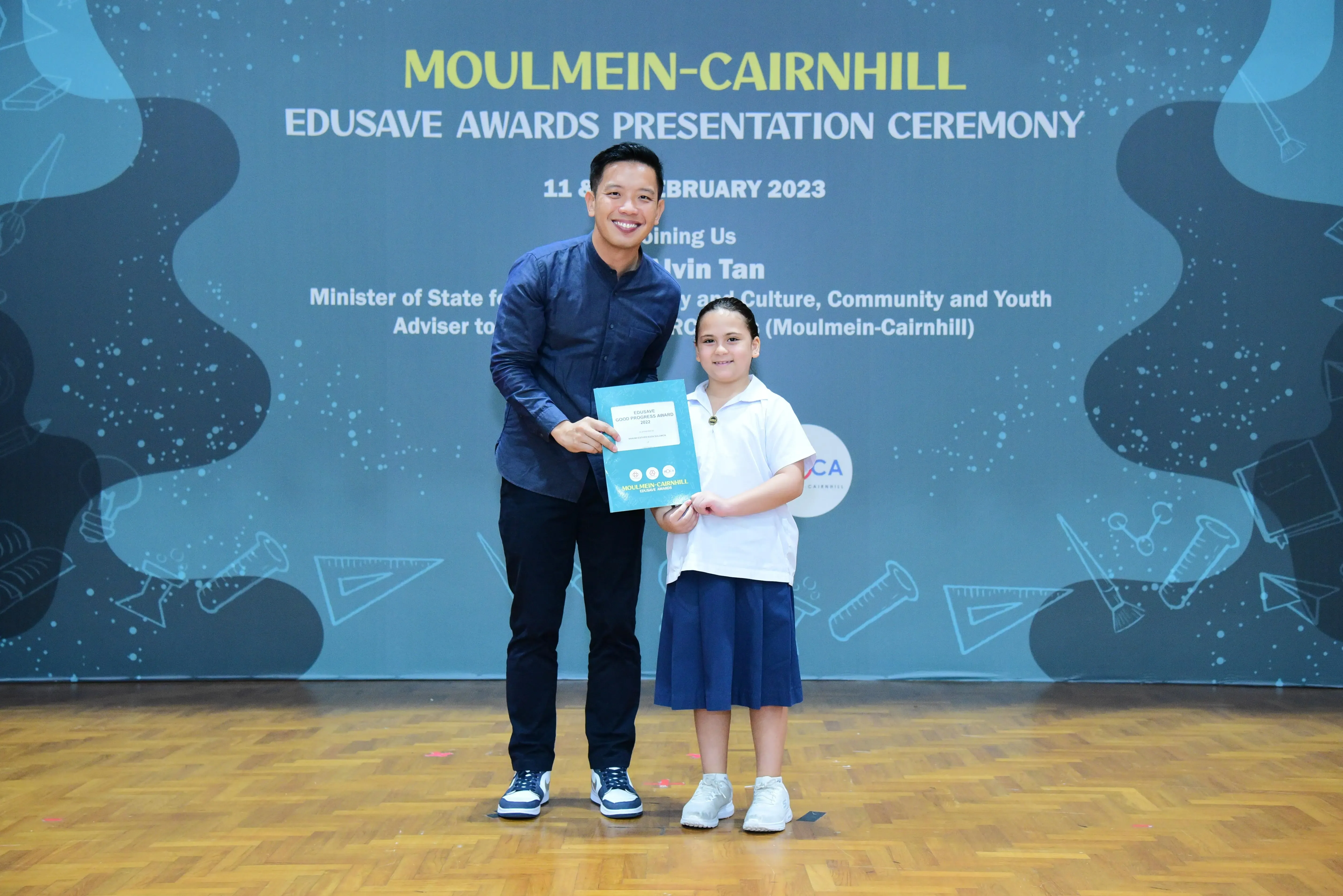 A man and a young girl hold a certificate together at the Moulmein-Cairnhill Edusave Awards Ceremony 2023.