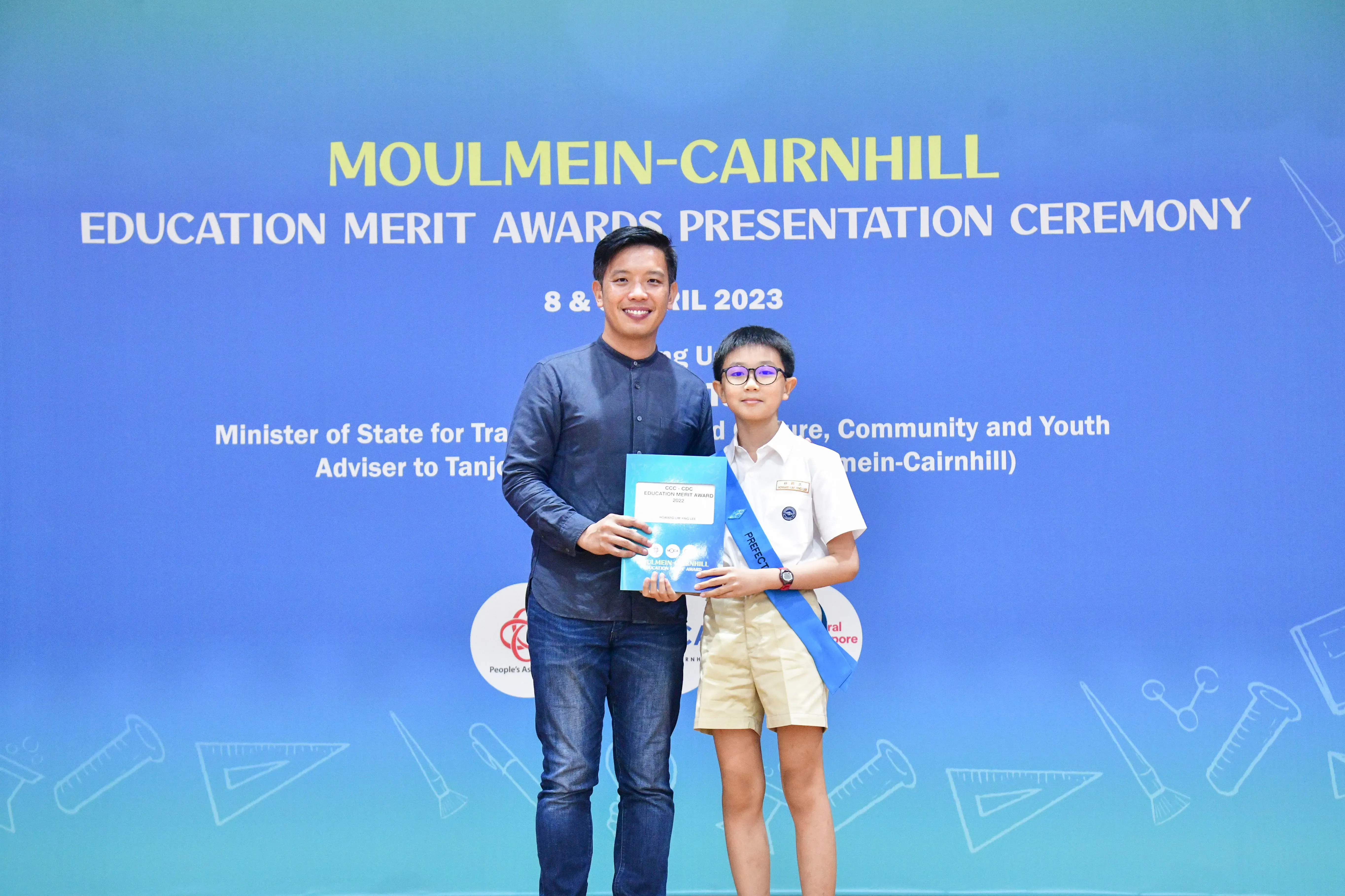 A man and a young boy in school uniform hold an award certificate at the Moulmein-Cairnhill Education Merit Awards 2023.