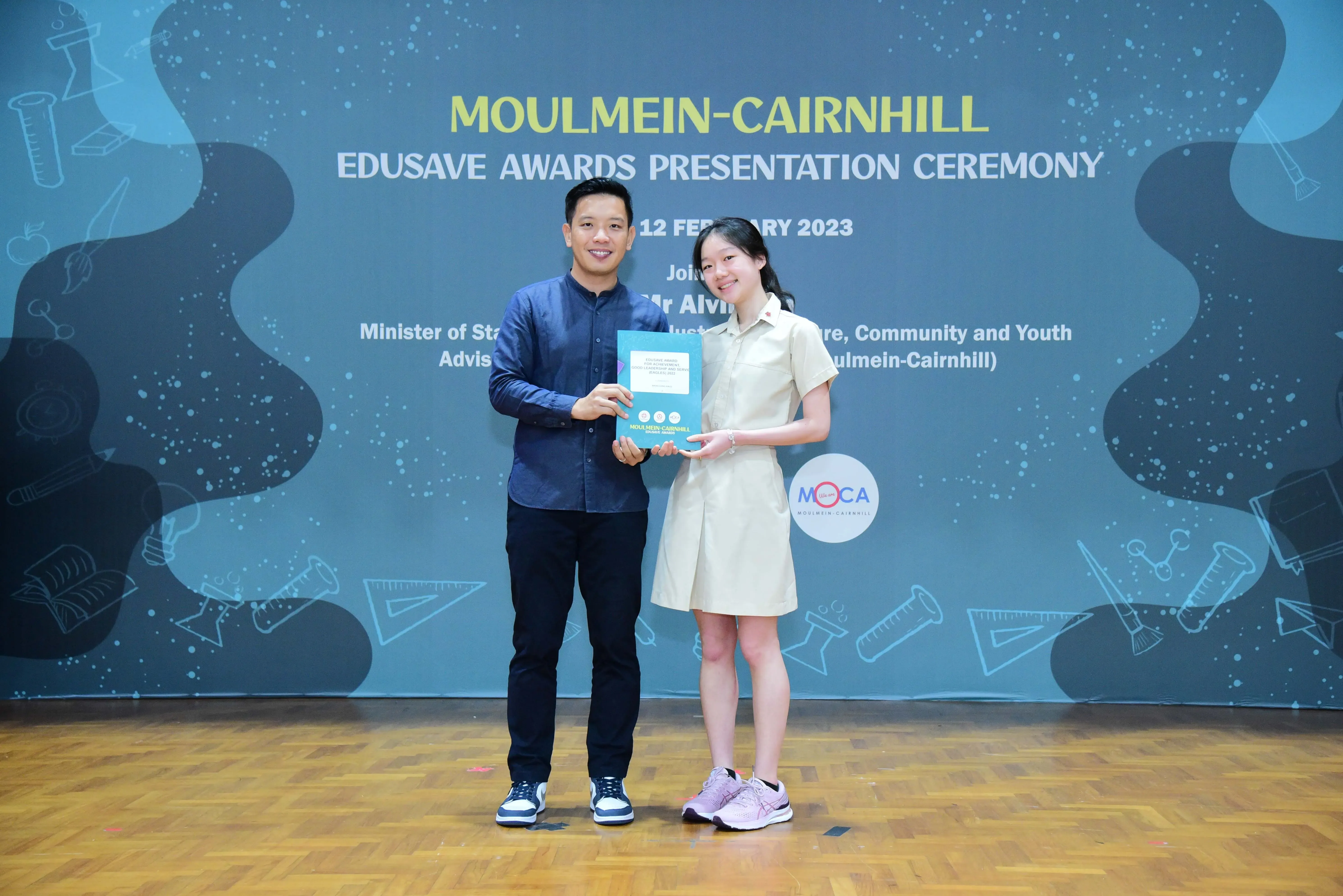 A man and a young girl hold a certificate together at the Moulmein-Cairnhill Edusave Awards Ceremony, February 2023.