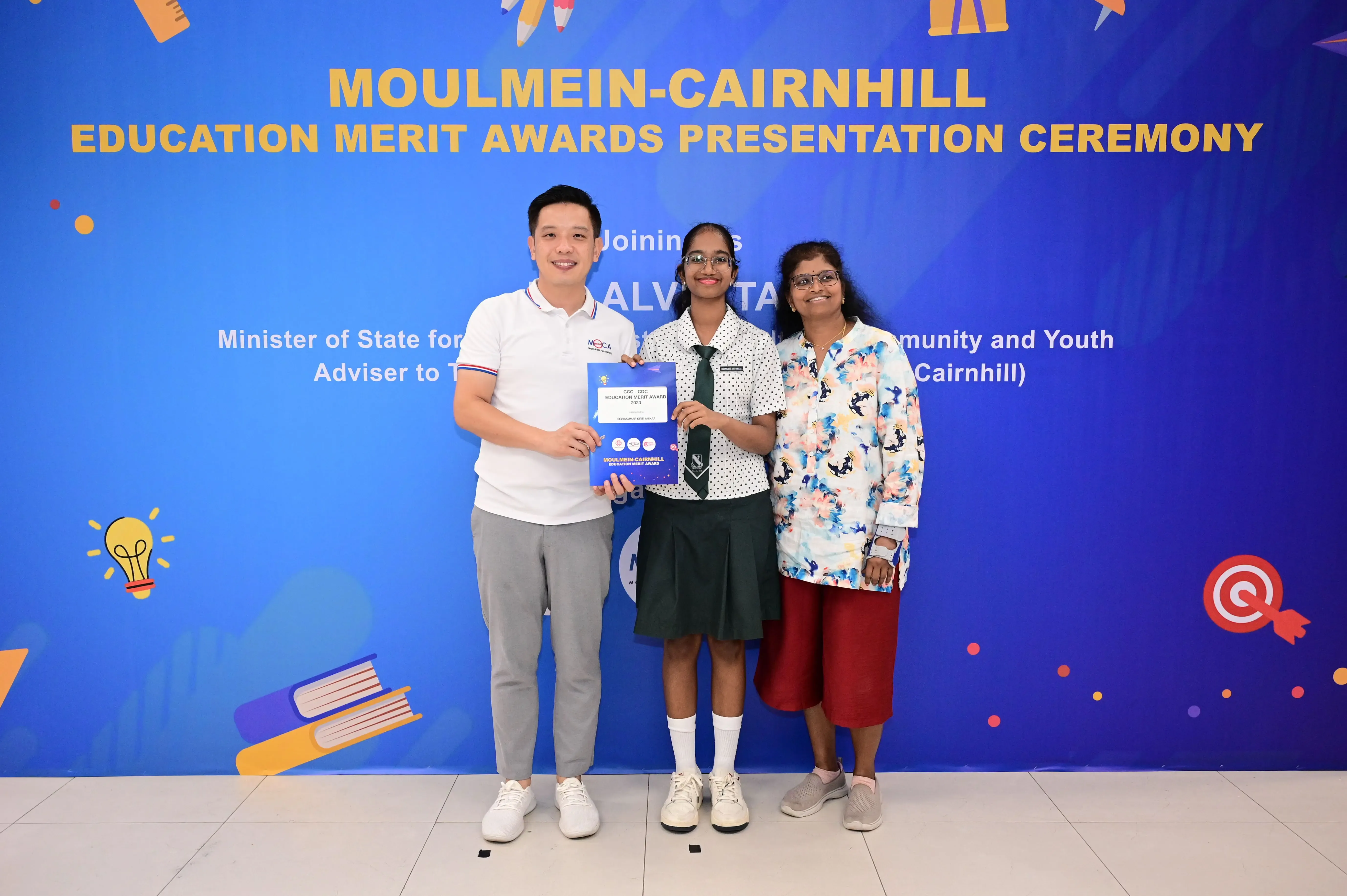 Three people pose holding an award certificate at the Moulmein-Cairnhill Education Merit Awards Presentation Ceremony.