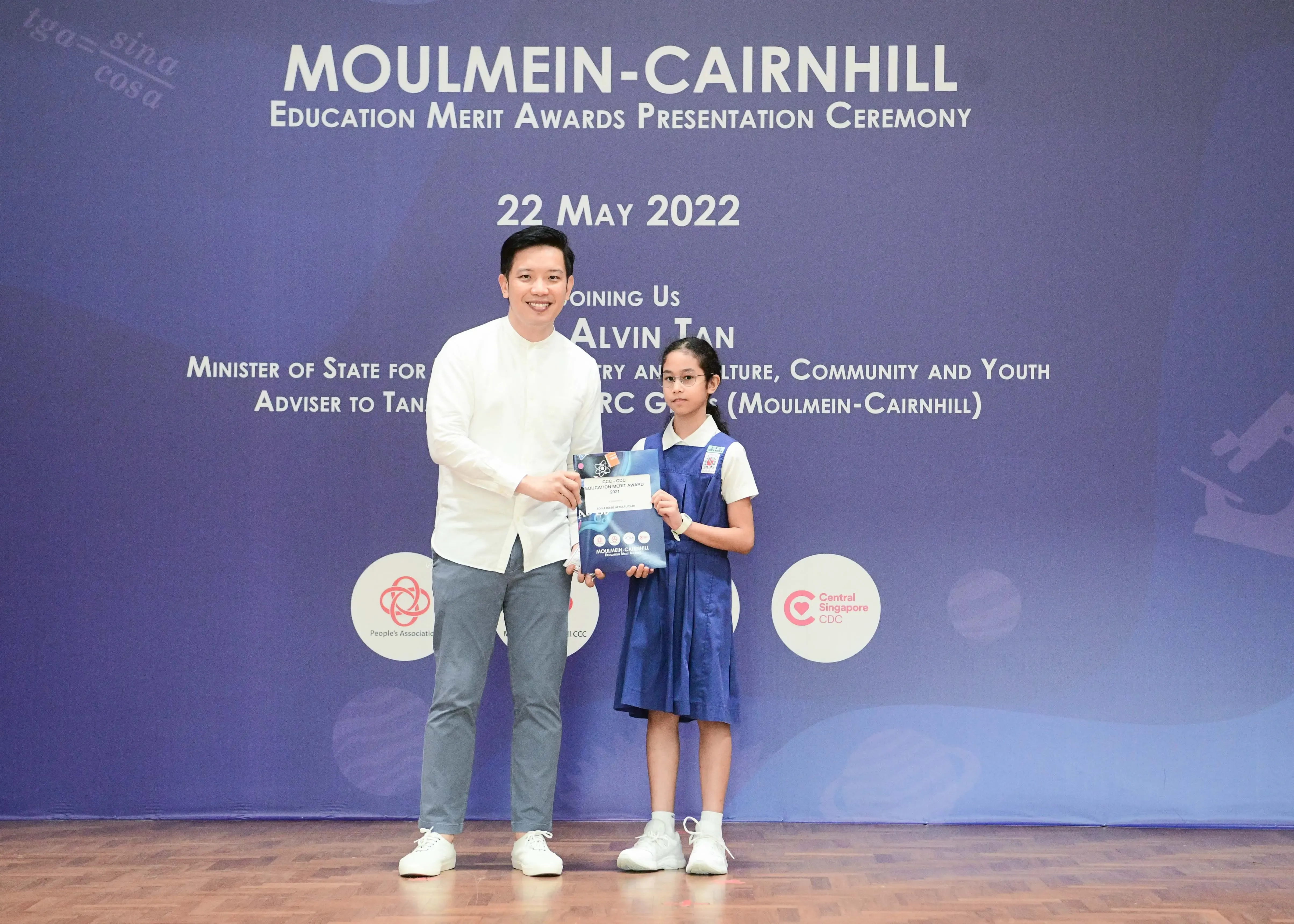 A man and a young girl in school uniform hold an award at the Moulmein-Cairnhill Education Merit Awards ceremony on 22 May 2022.