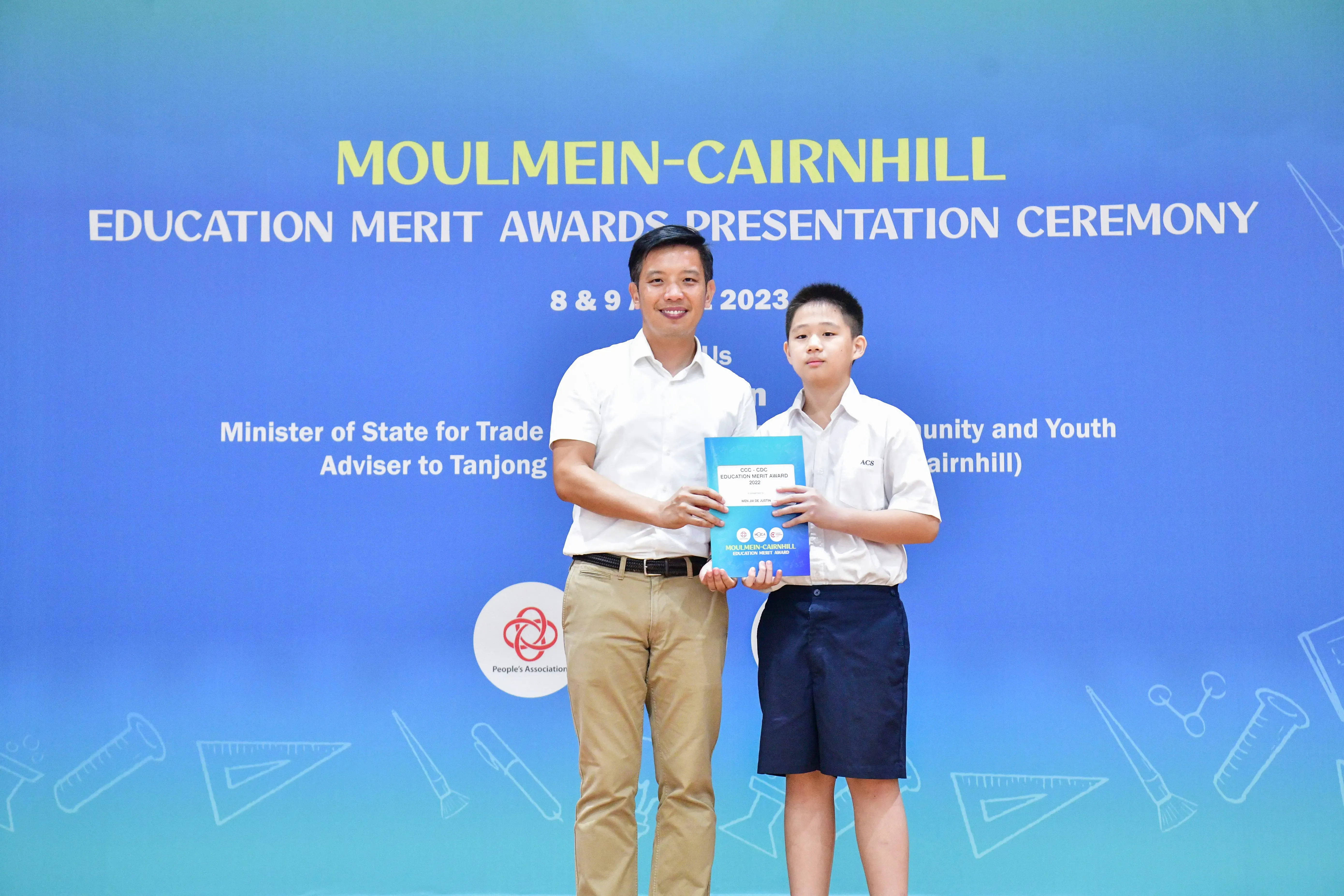 An adult man and a young boy hold an award together at the Moulmein-Cairnhill Education Merit Awards Ceremony 2023.