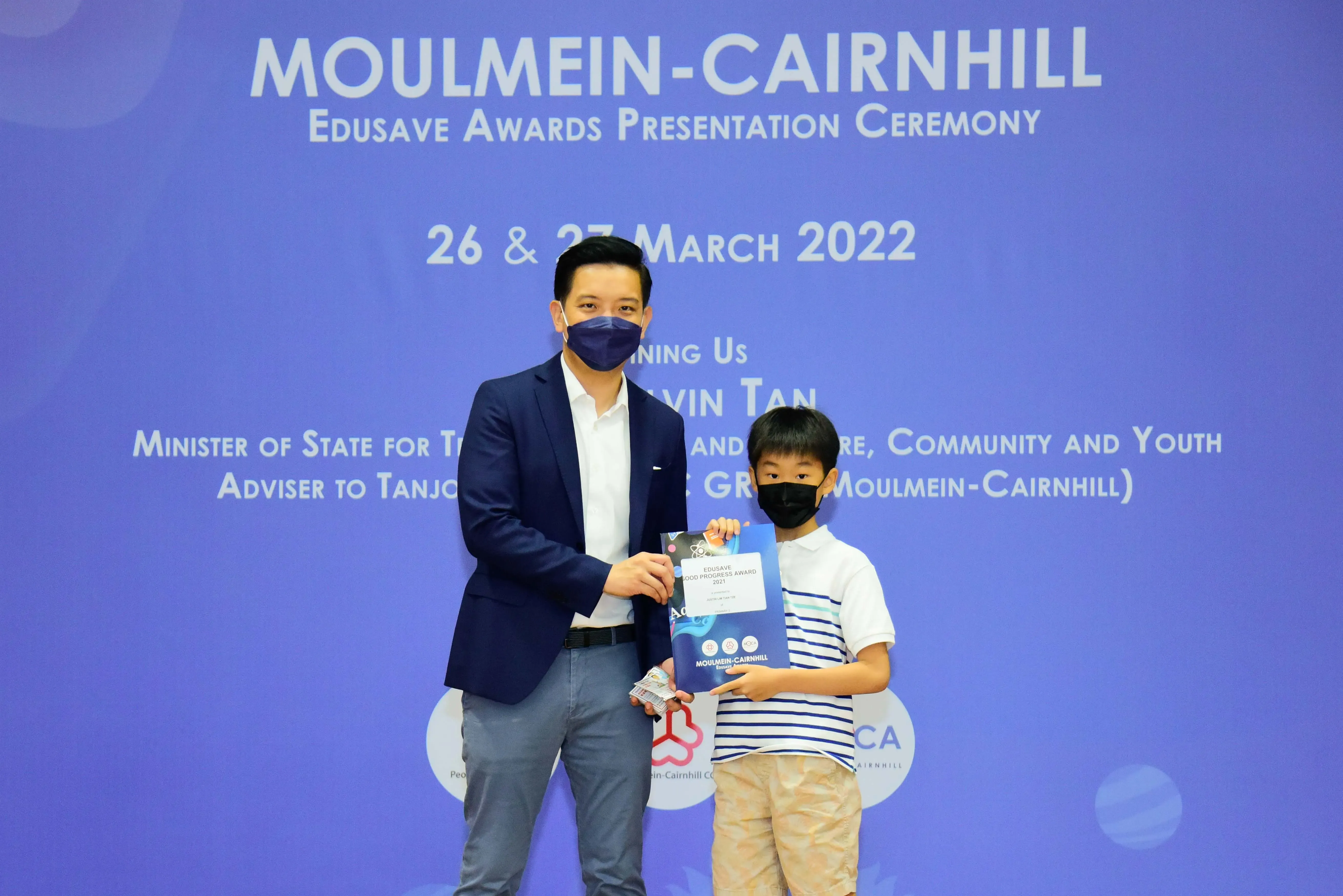 An adult and a child wearing masks hold an award certificate at the Moulmein-Cairnhill Edusave Awards Ceremony 2022.