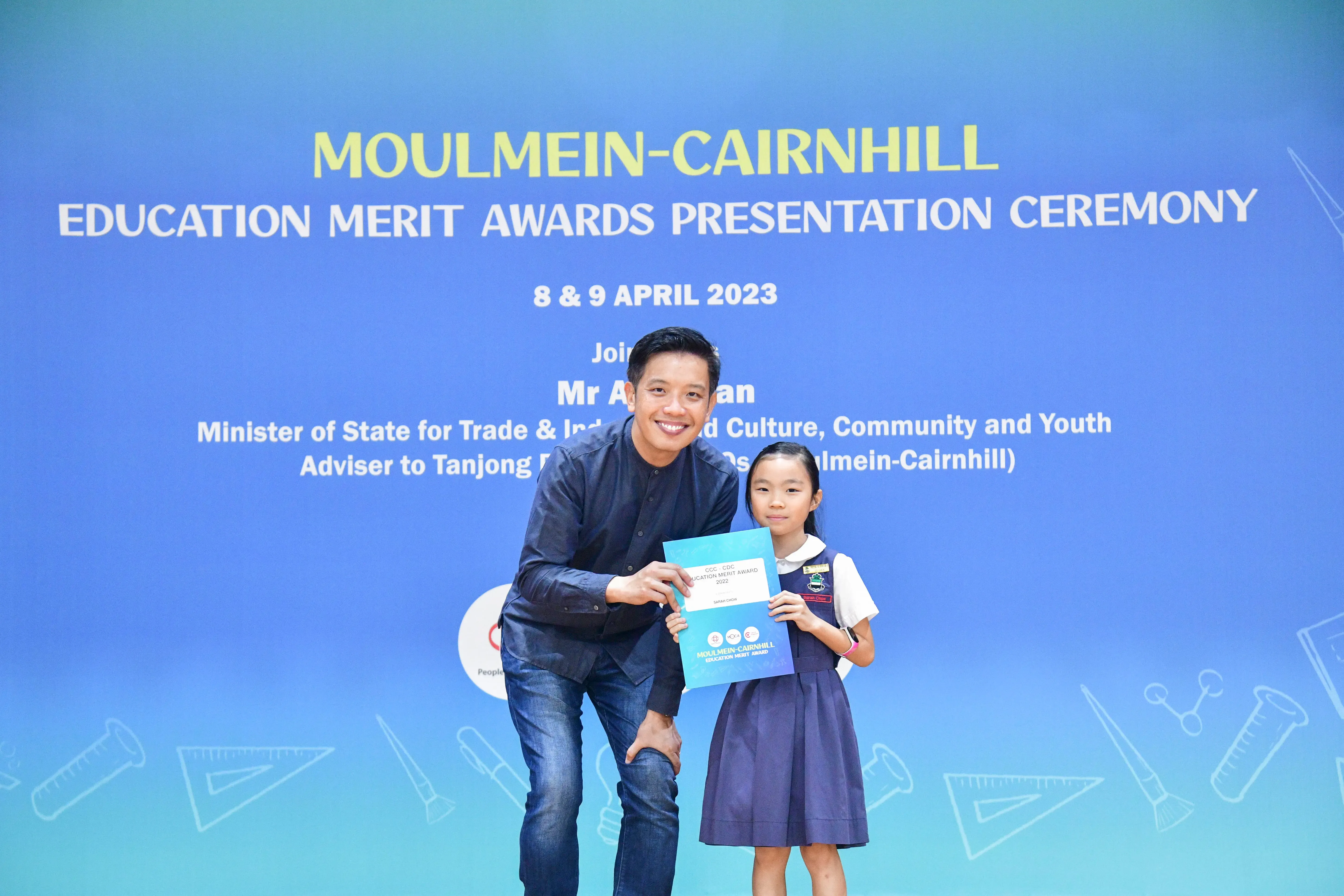 A man and a young girl hold an award certificate at the Moulmein-Cairnhill Education Merit Awards Ceremony, April 2023.