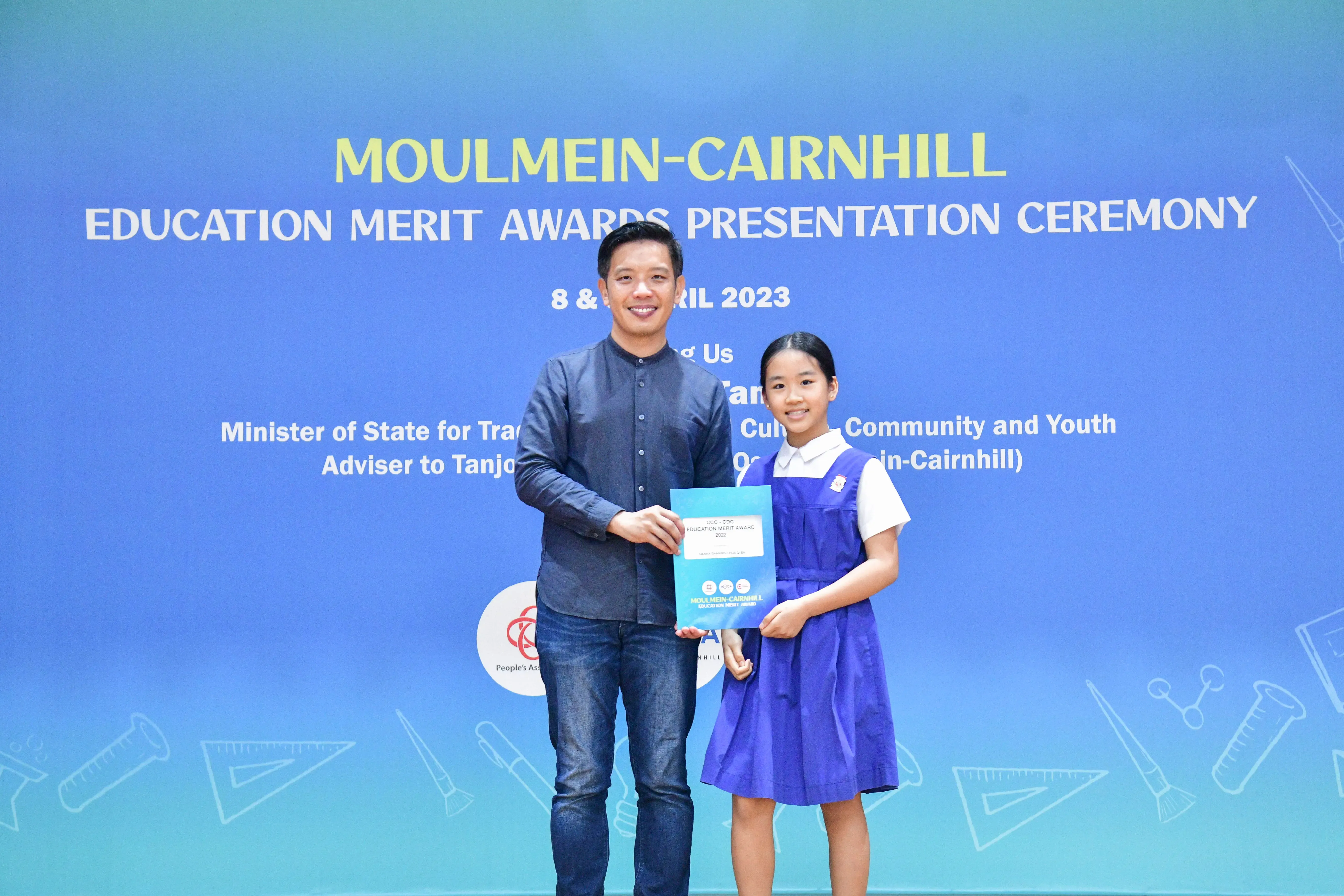 A man and a young girl in school uniform hold an award certificate at the Moulmein-Cairnhill Education Merit Awards 2023.