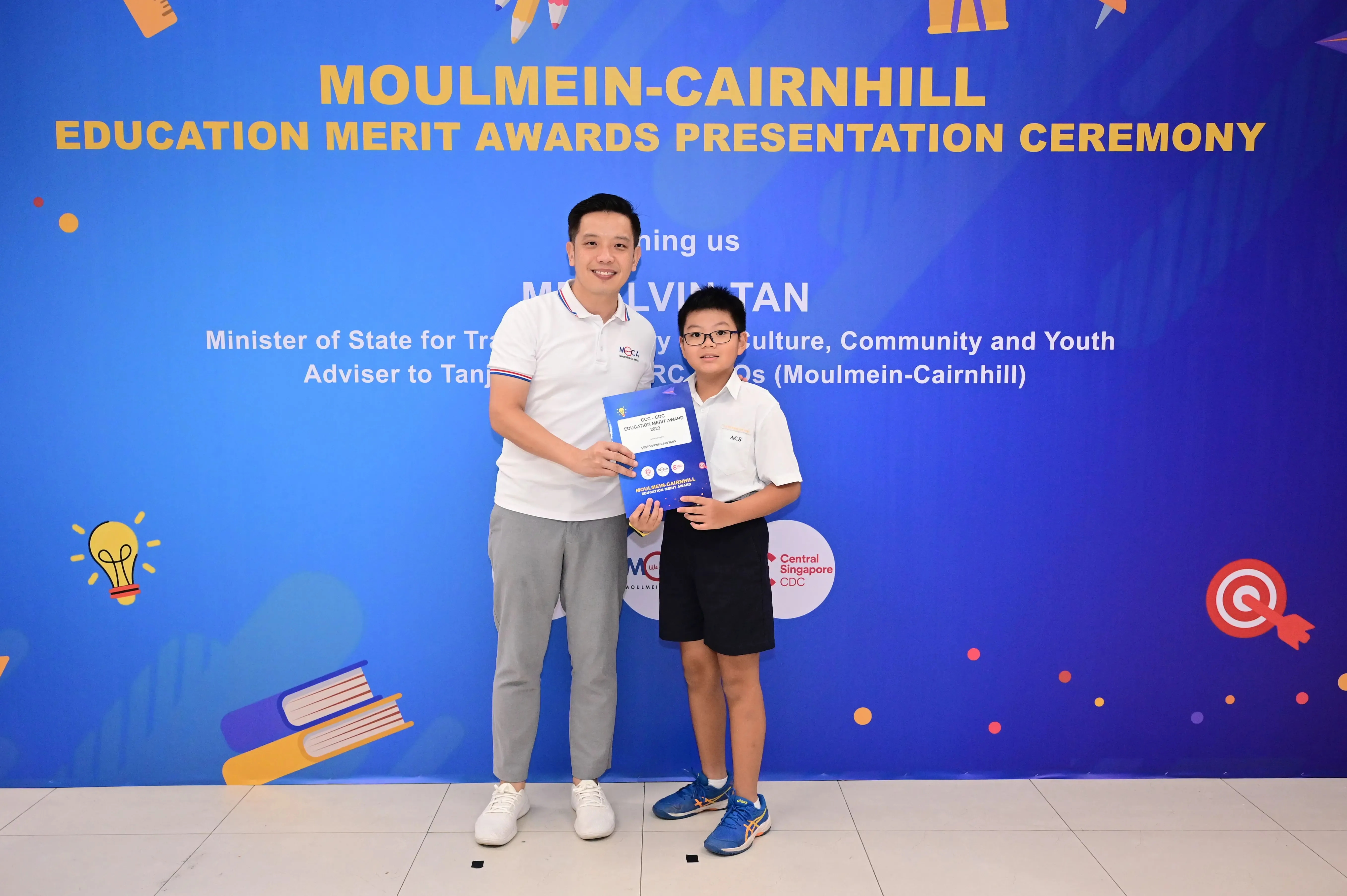 Man and young boy holding an award booklet at Moulmein-Cairnhill Education Merit Awards Presentation Ceremony.