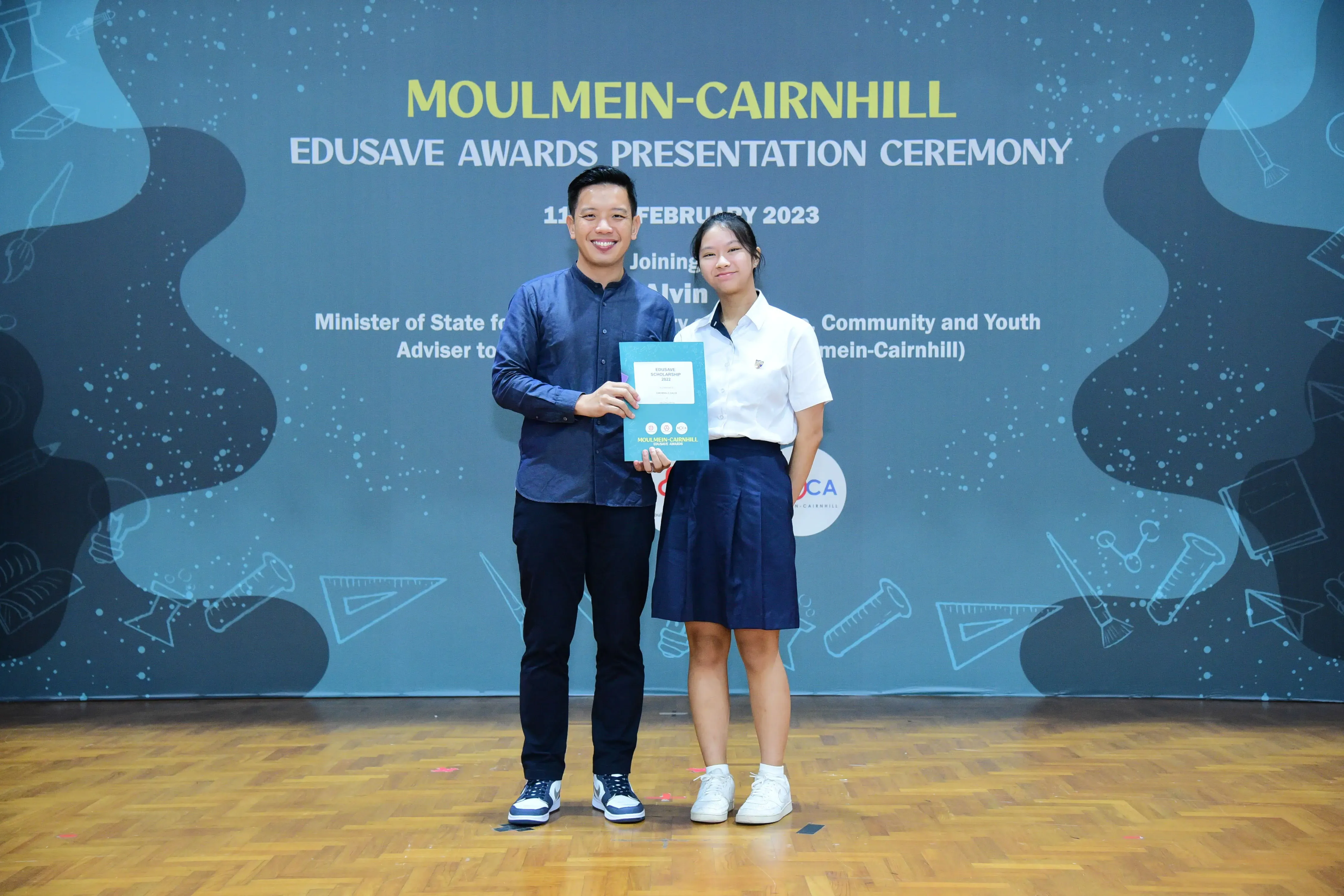 A man and a female student hold a certificate at the Moulmein-Cairnhill Edusave Awards Ceremony, February 2023.