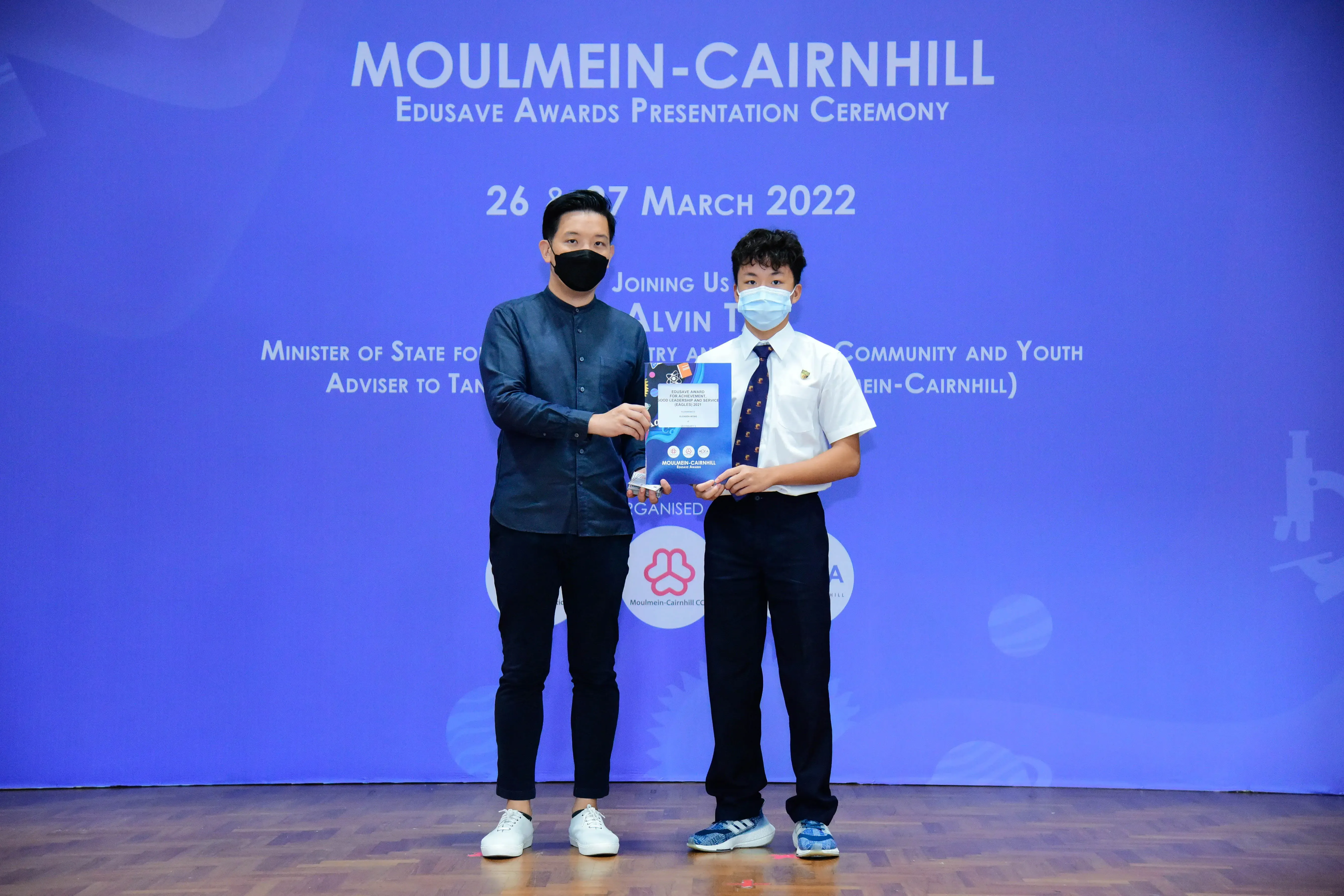 Two masked individuals hold an award certificate at the Moulmein-Cairnhill Edusave Awards Ceremony, March 2022.