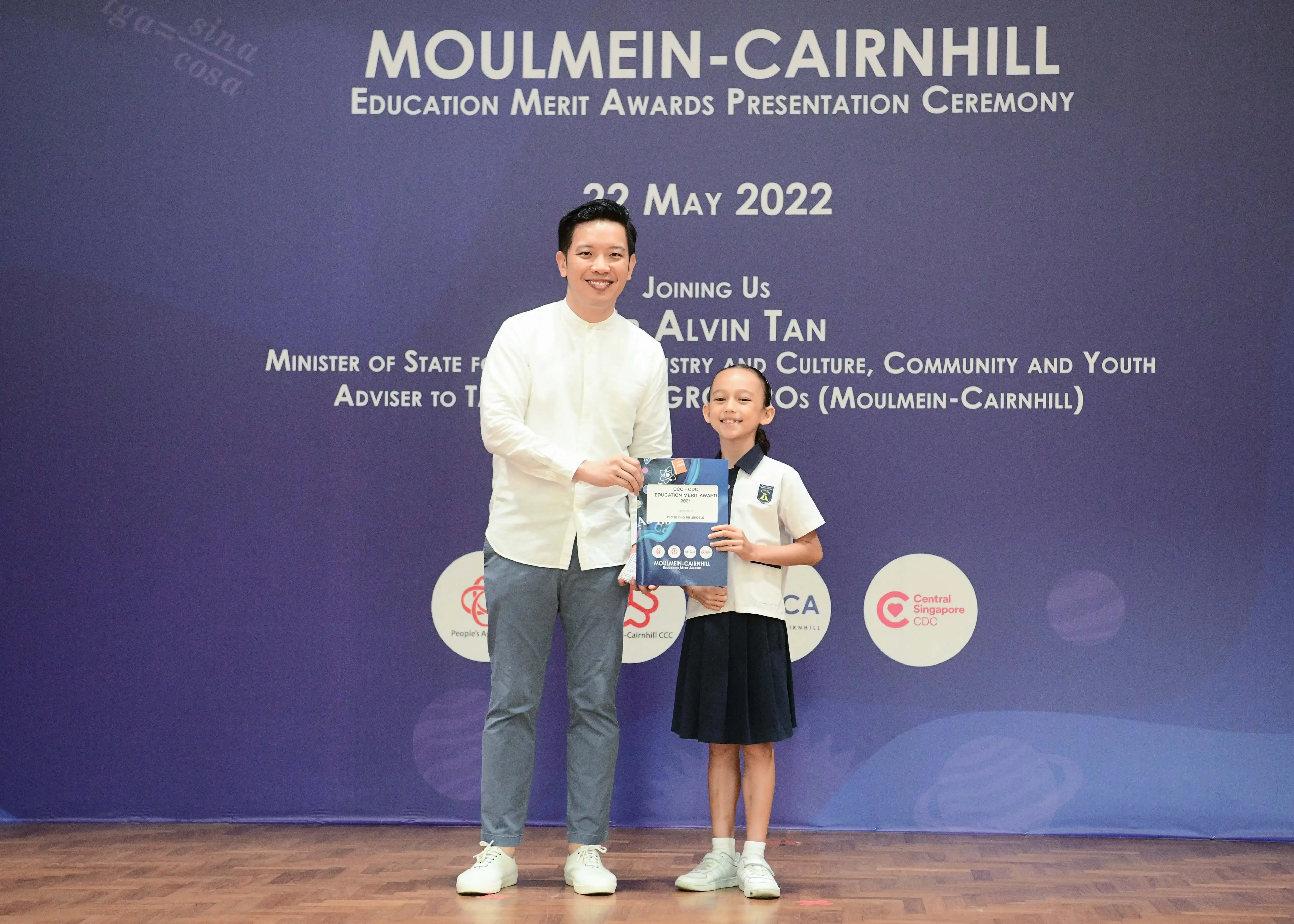 Man and young girl in school uniform hold an award booklet at Moulmein-Cairnhill Education Merit Awards, May 2022.
