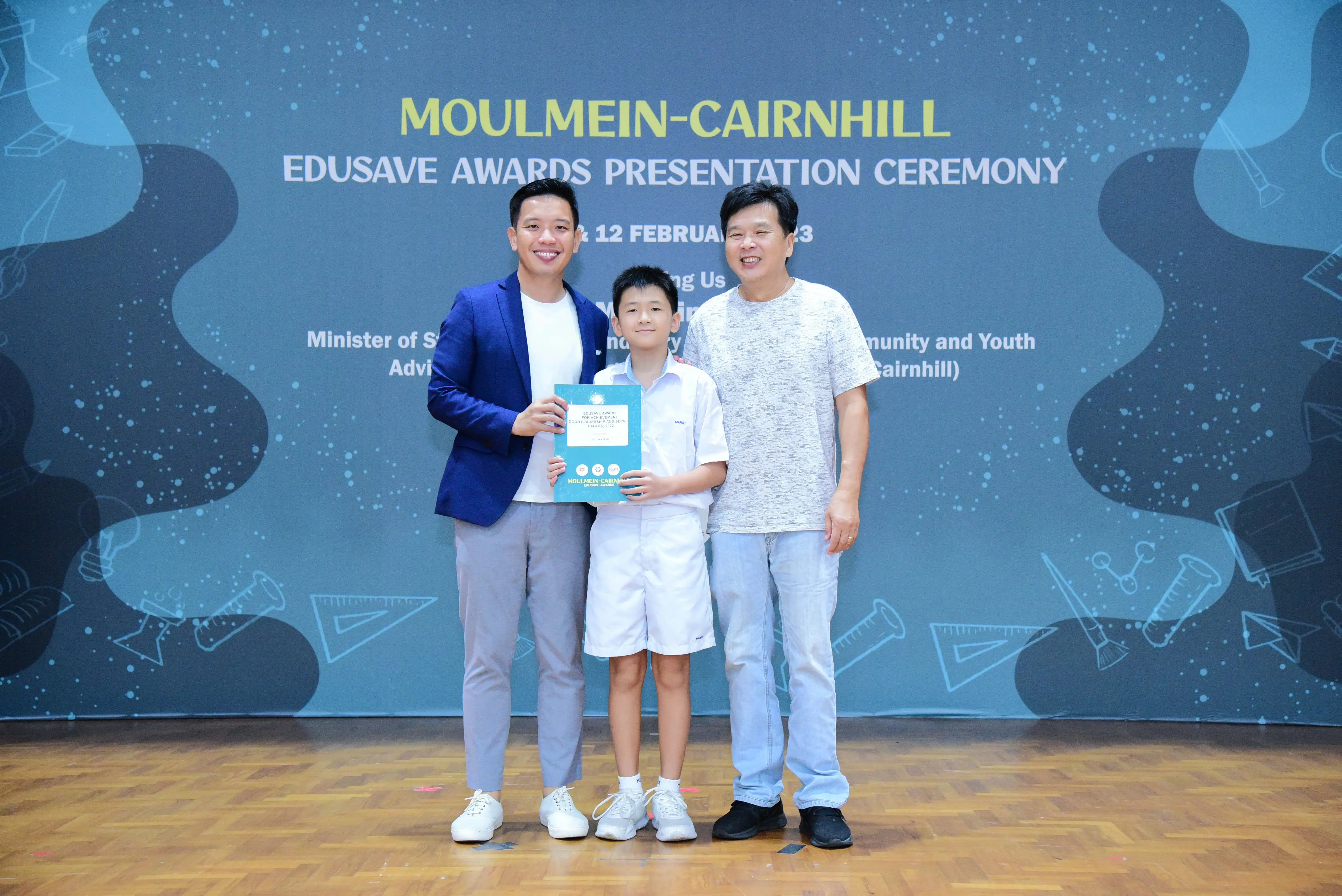 Two men and a boy holding a certificate pose at the Moulmein-Cairnhill Edusave Awards Presentation Ceremony.