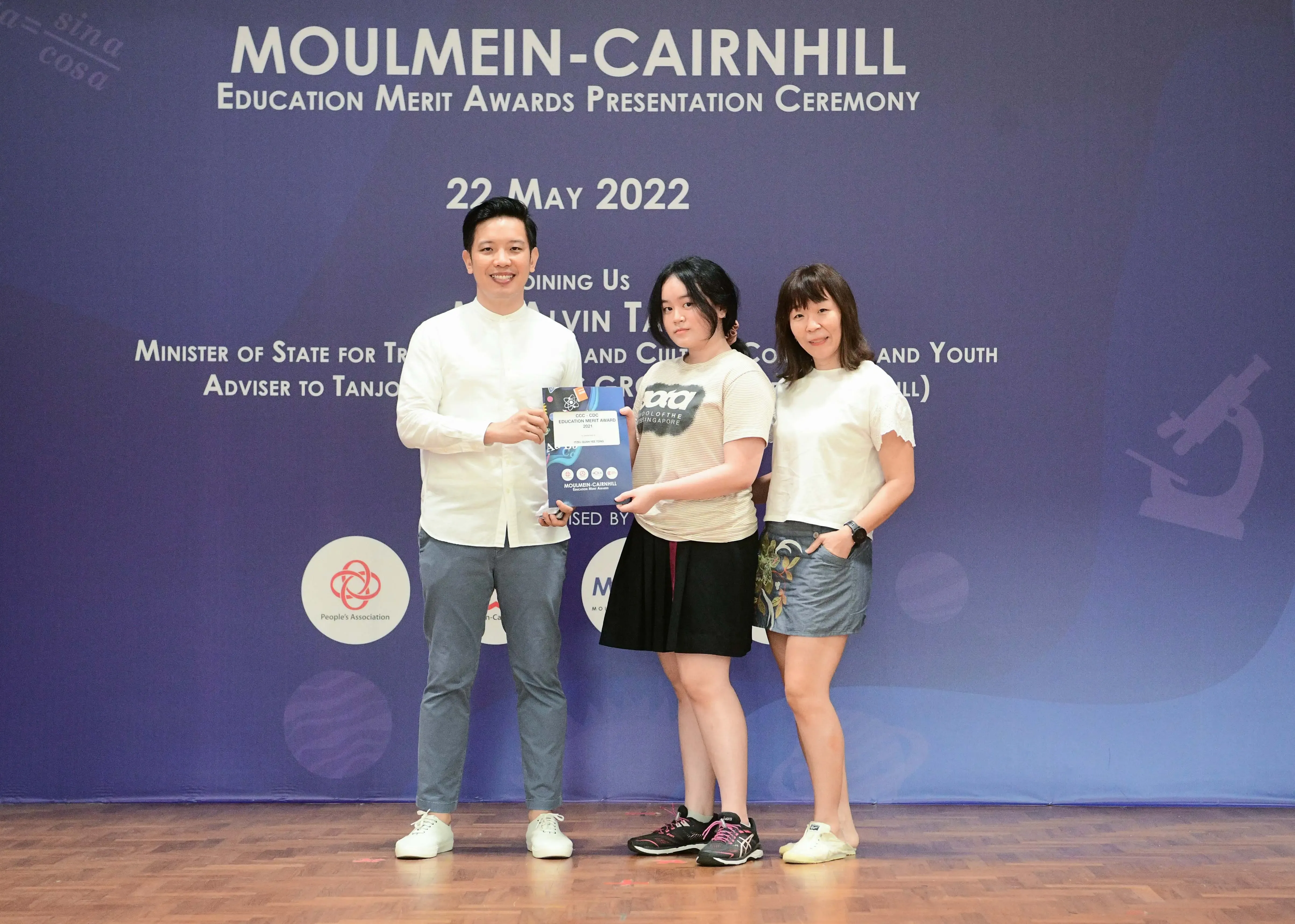 Three people pose on a stage at the Moulmein-Cairnhill Education Merit Awards Presentation Ceremony on 22 May 2022.