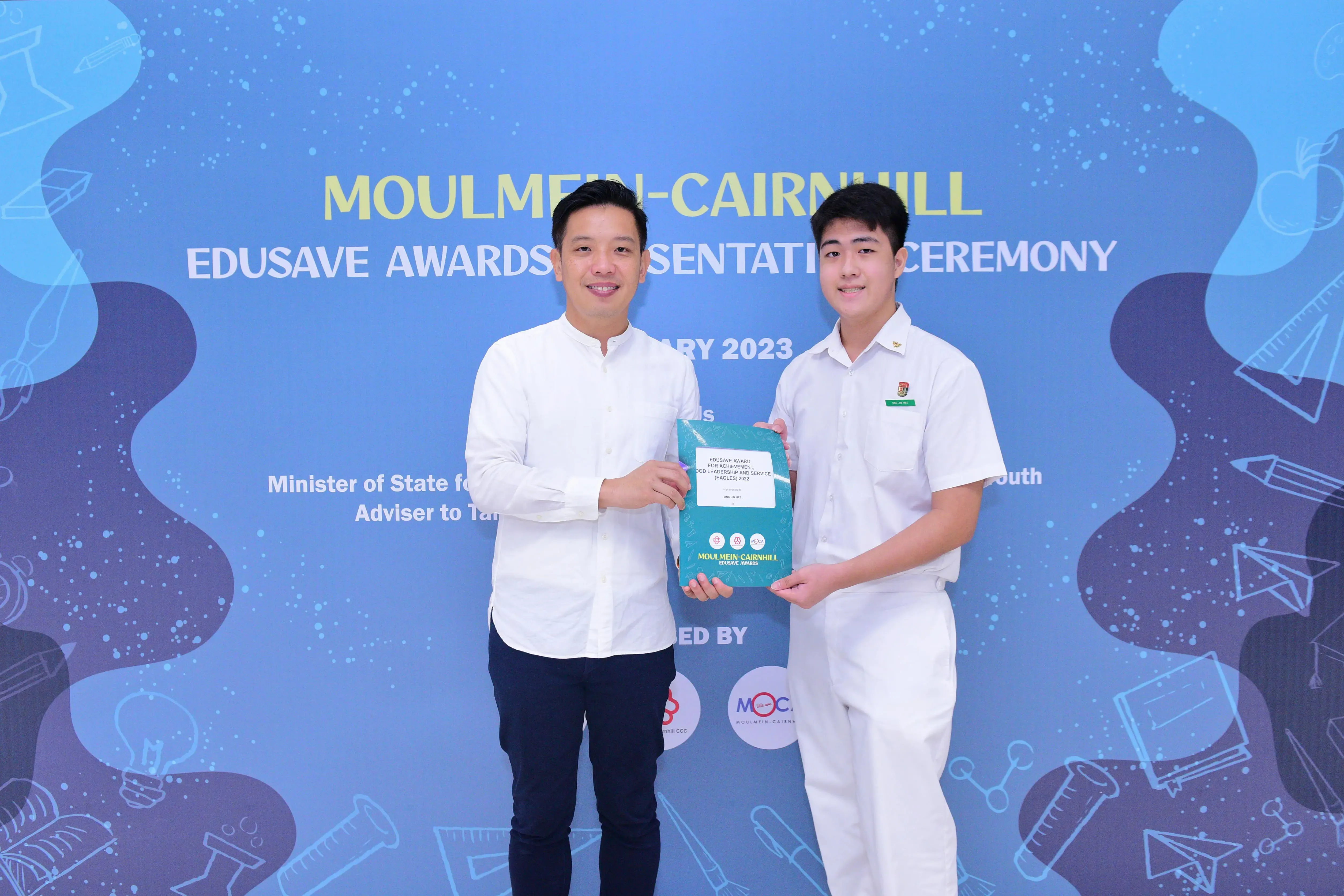 Two men smile while holding an award folder at the Moulmein-Cairnhill Edusave Awards Ceremony 2023.