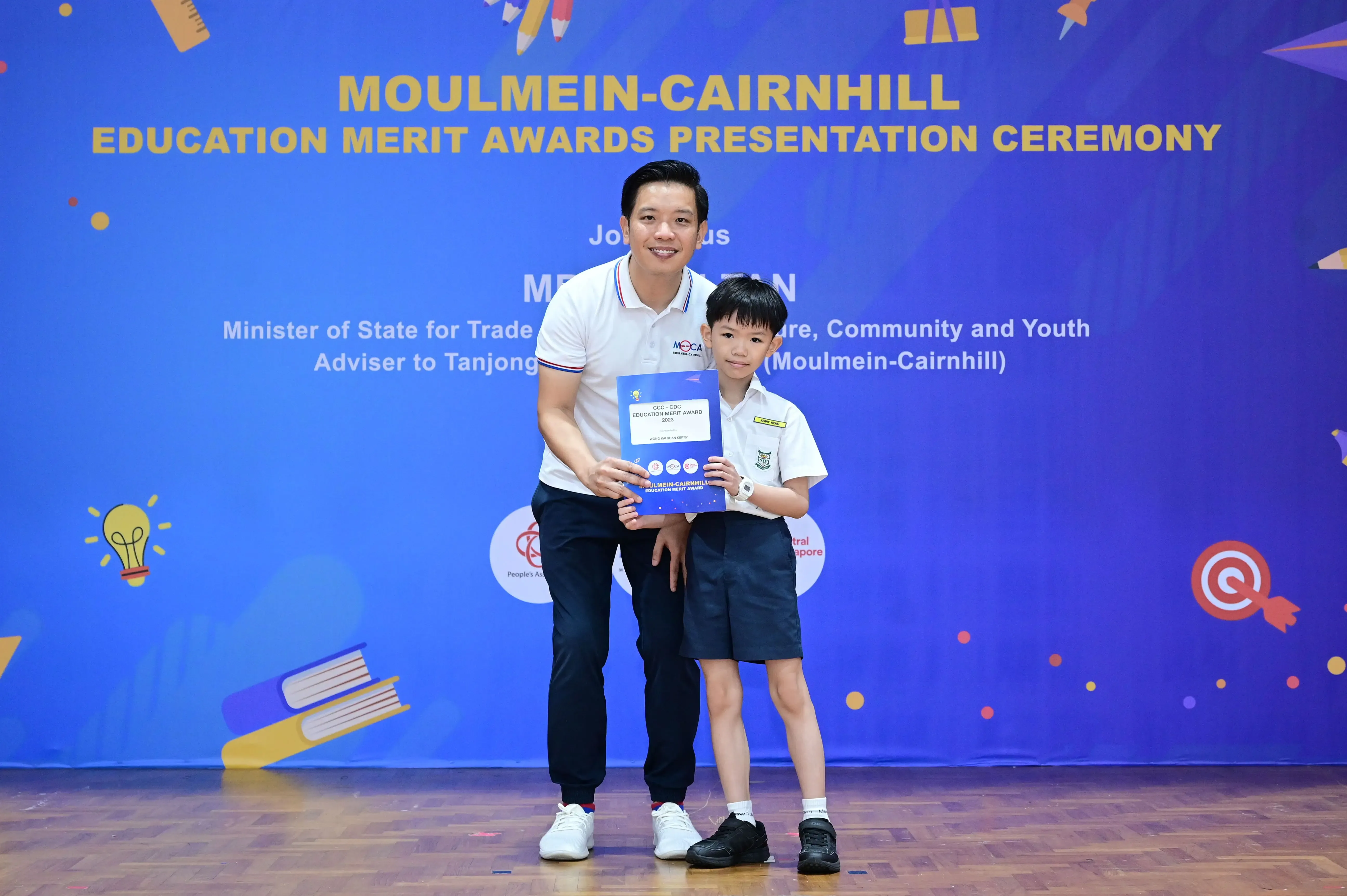 A man and a young boy hold an award certificate at the Moulmein-Cairnhill Education Merit Awards Presentation Ceremony.