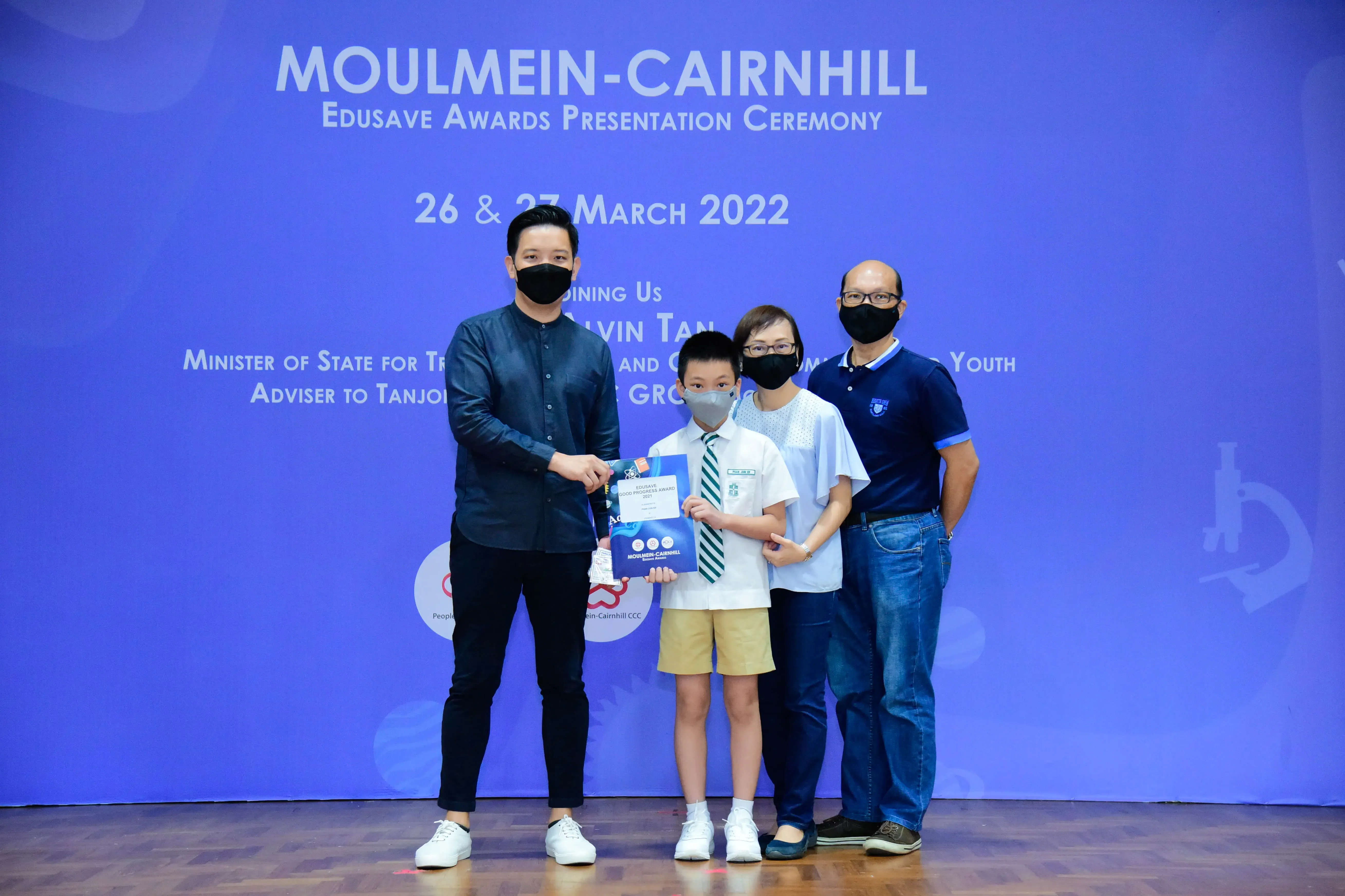 Four masked people pose at Moulmein-Cairnhill Edusave Awards Presentation Ceremony, March 2022, holding a certificate.