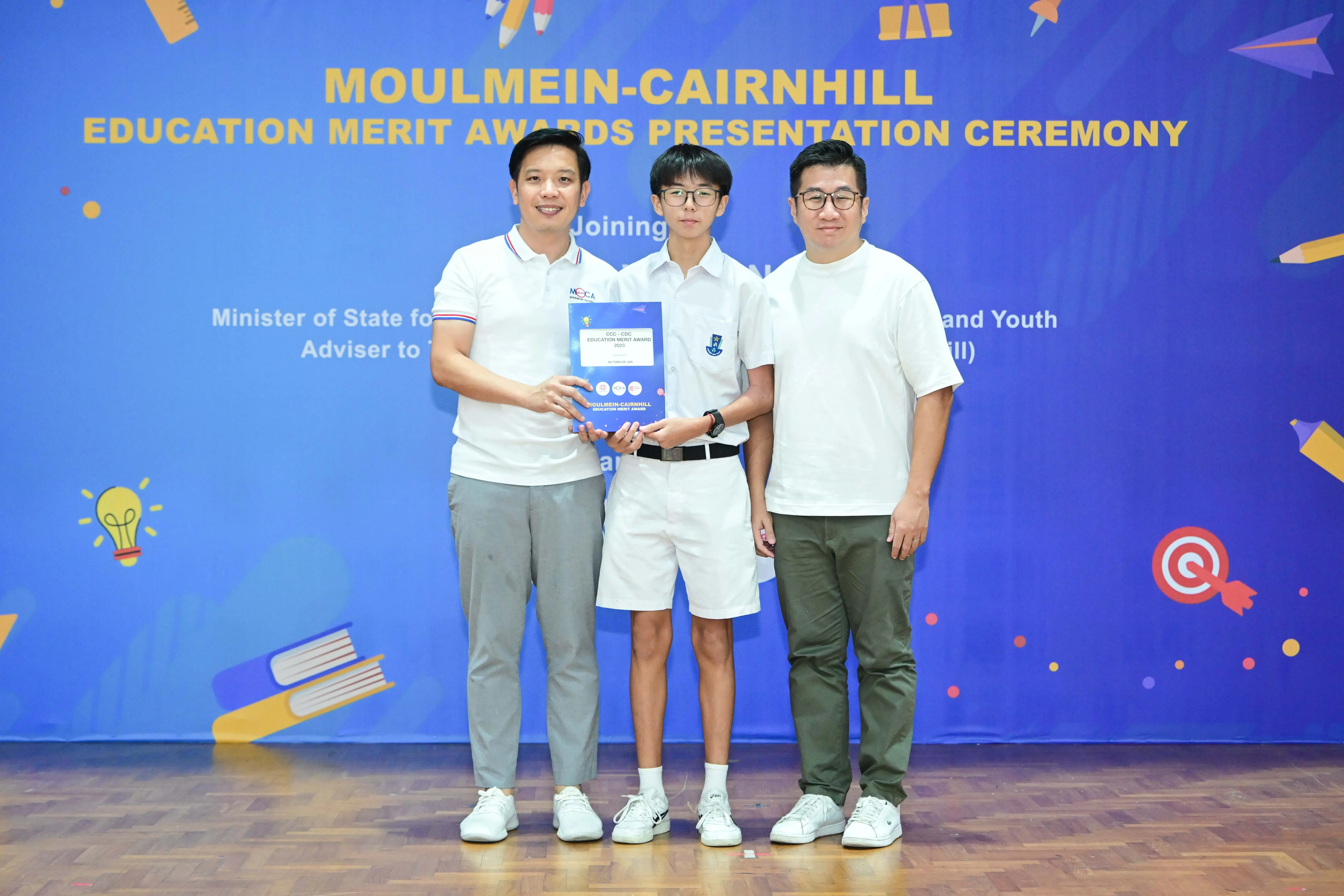 Three people pose at the Moulmein-Cairnhill Education Merit Awards Presentation Ceremony, with a student holding a certificate.