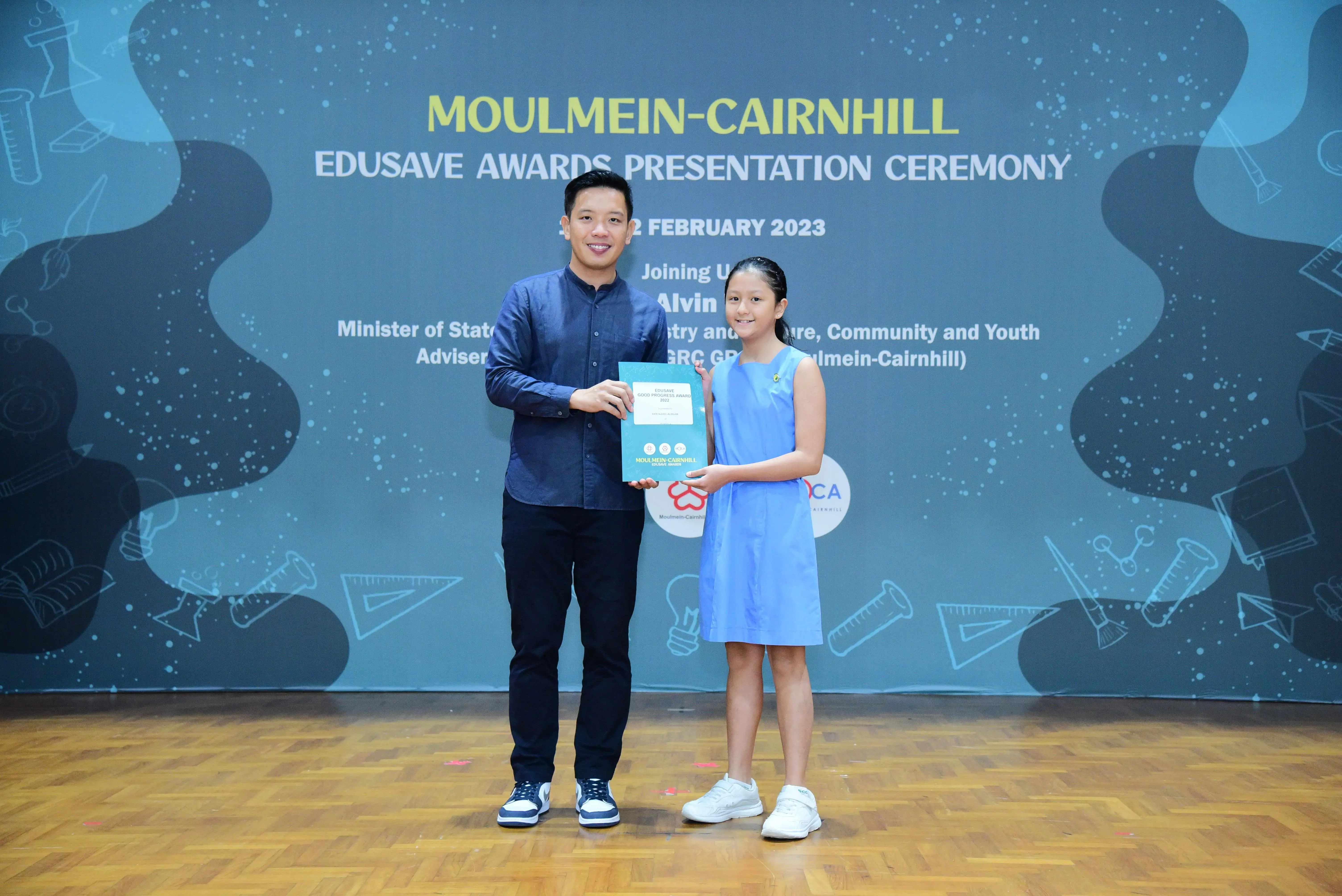 A man and a young girl hold a certificate at the Moulmein-Cairnhill Edusave Awards Presentation Ceremony, February 2023.