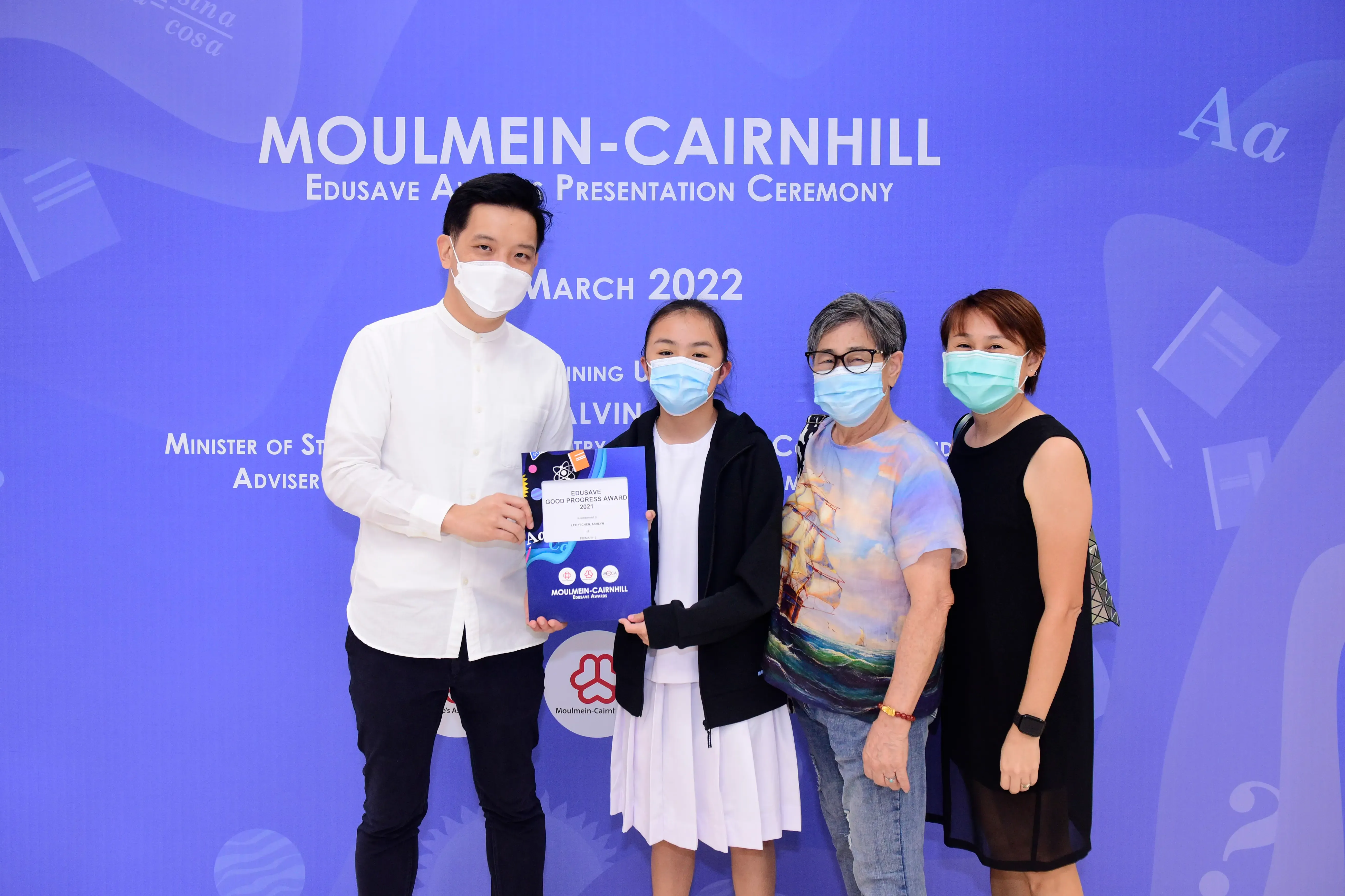 Four masked people pose at the Moulmein-Cairnhill Edusave Awards Ceremony March 2022, holding an award folder.