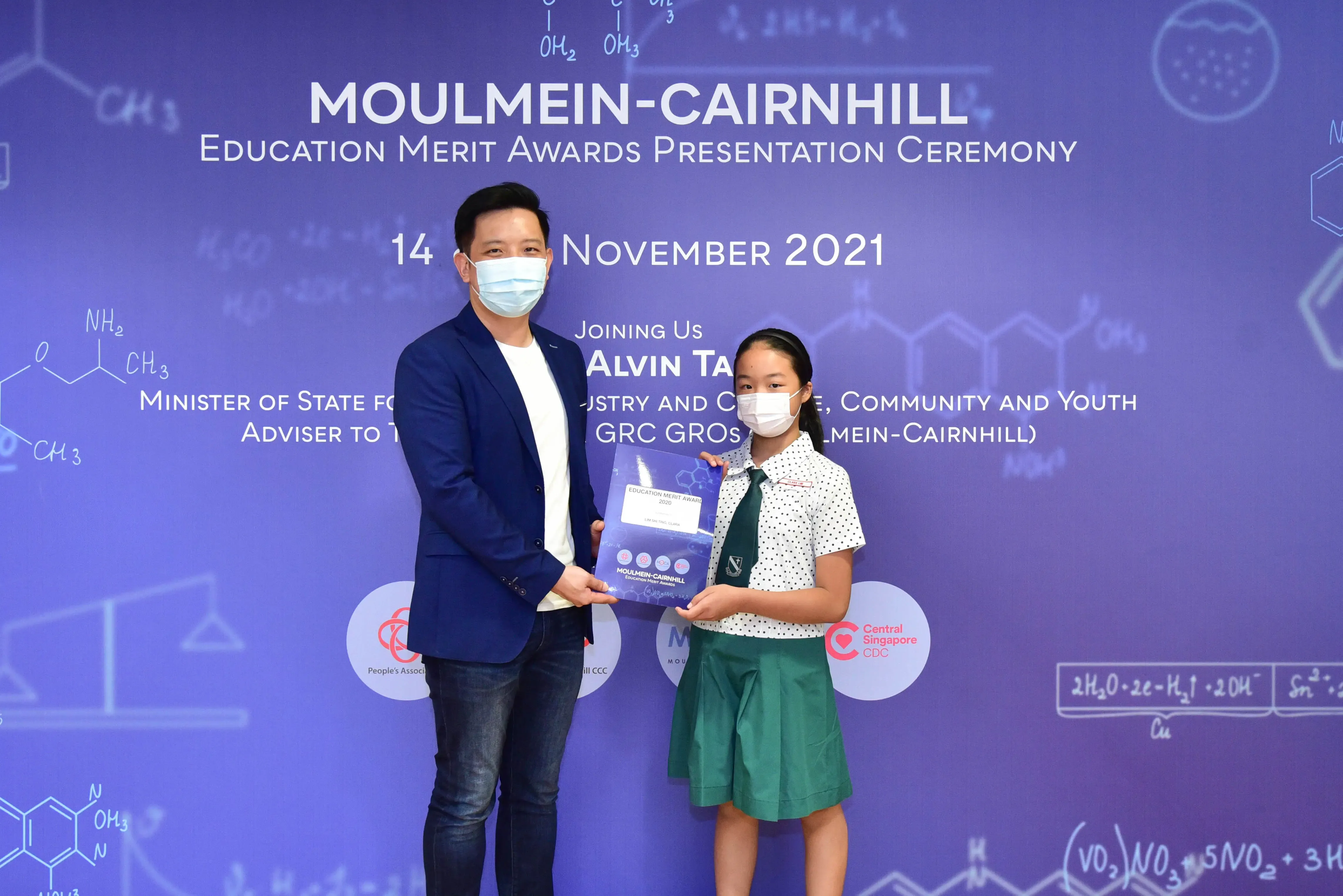 A man and a young girl in school uniform hold a certificate at the Moulmein-Cairnhill Education Merit Awards 2021.