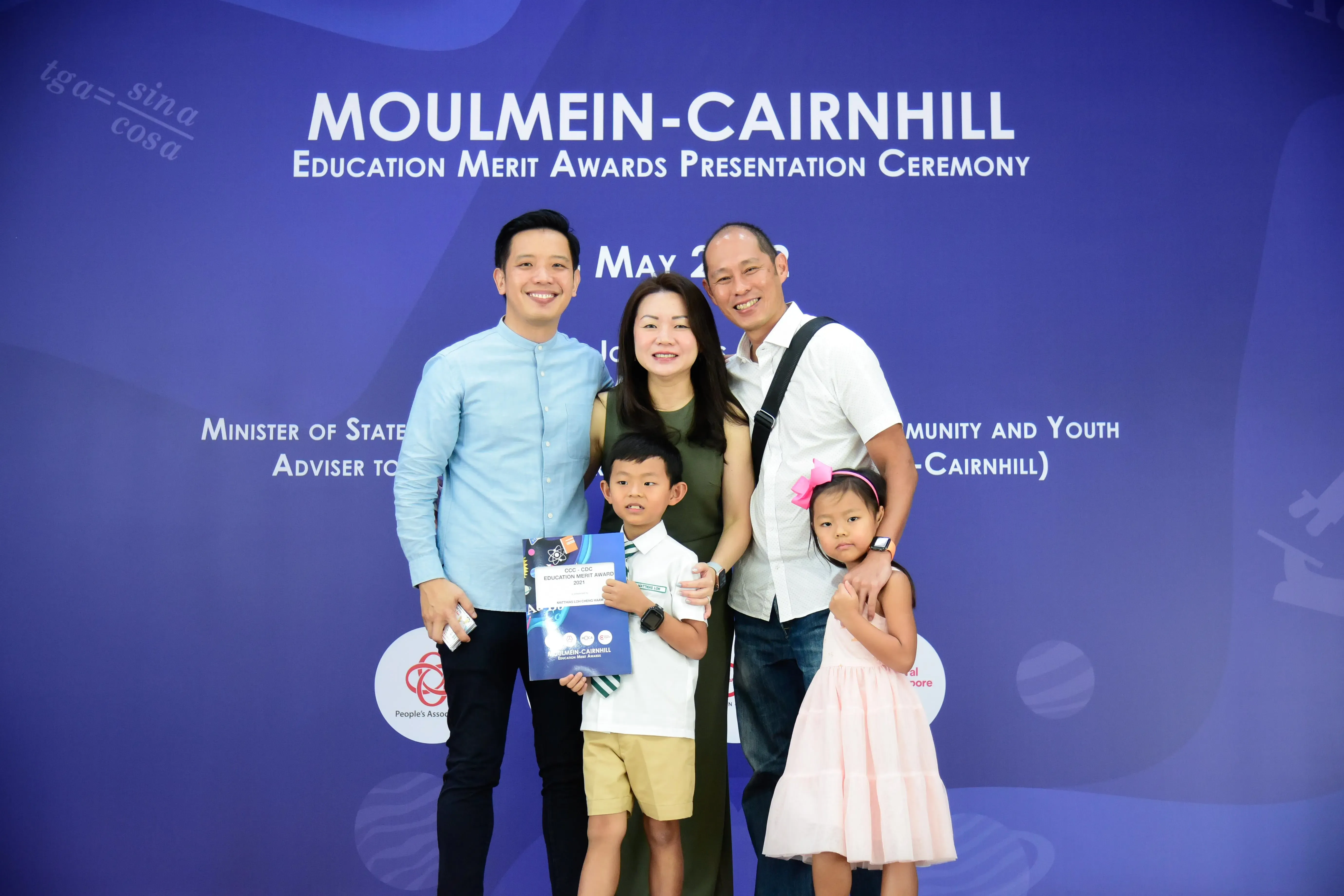 Family of four with a young boy holding an award certificate pose at the Moulmein-Cairnhill Education Merit Awards ceremony.