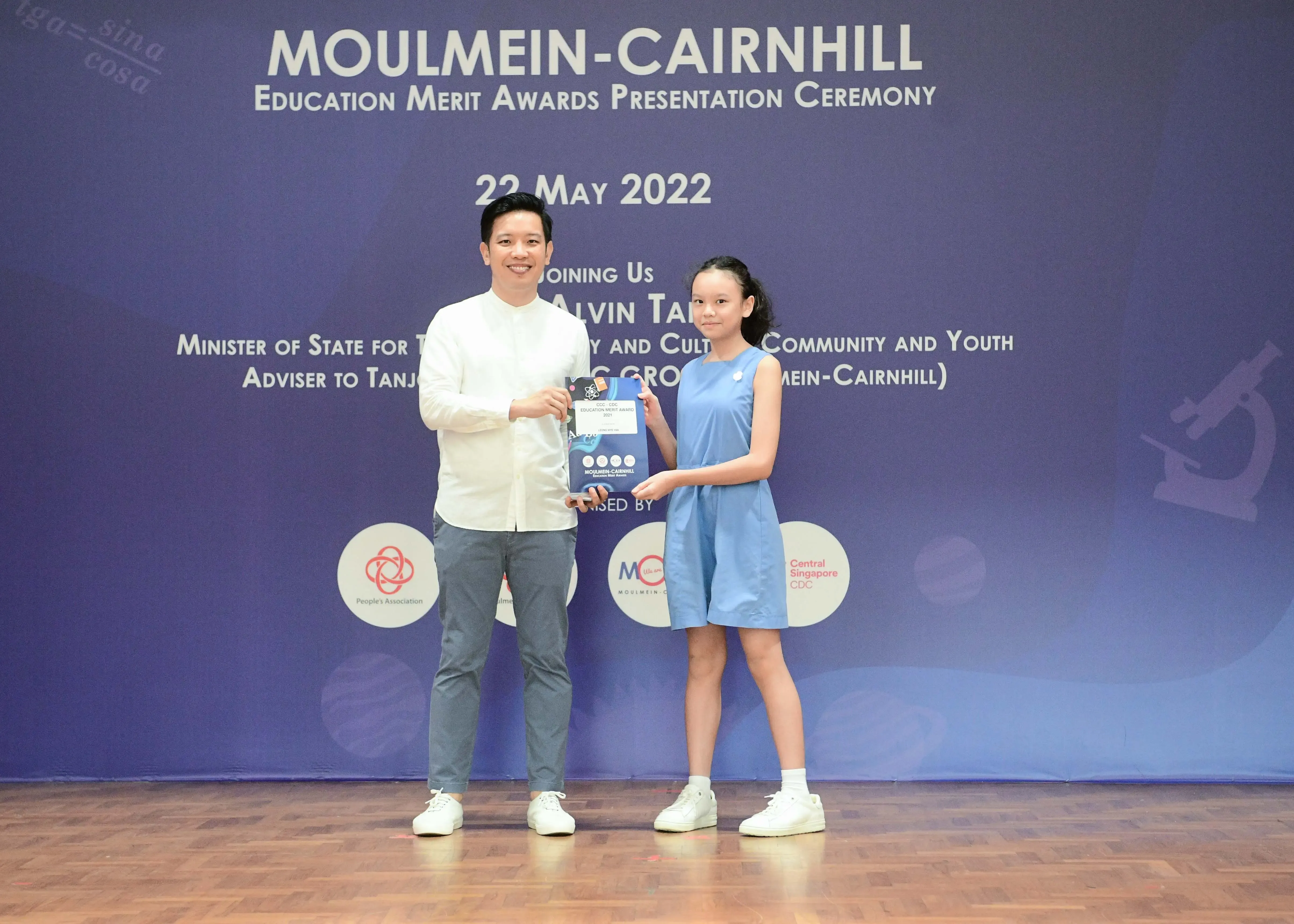 A man and a young girl hold an award together at the Moulmein-Cairnhill Education Merit Awards Ceremony on 22 May 2022.