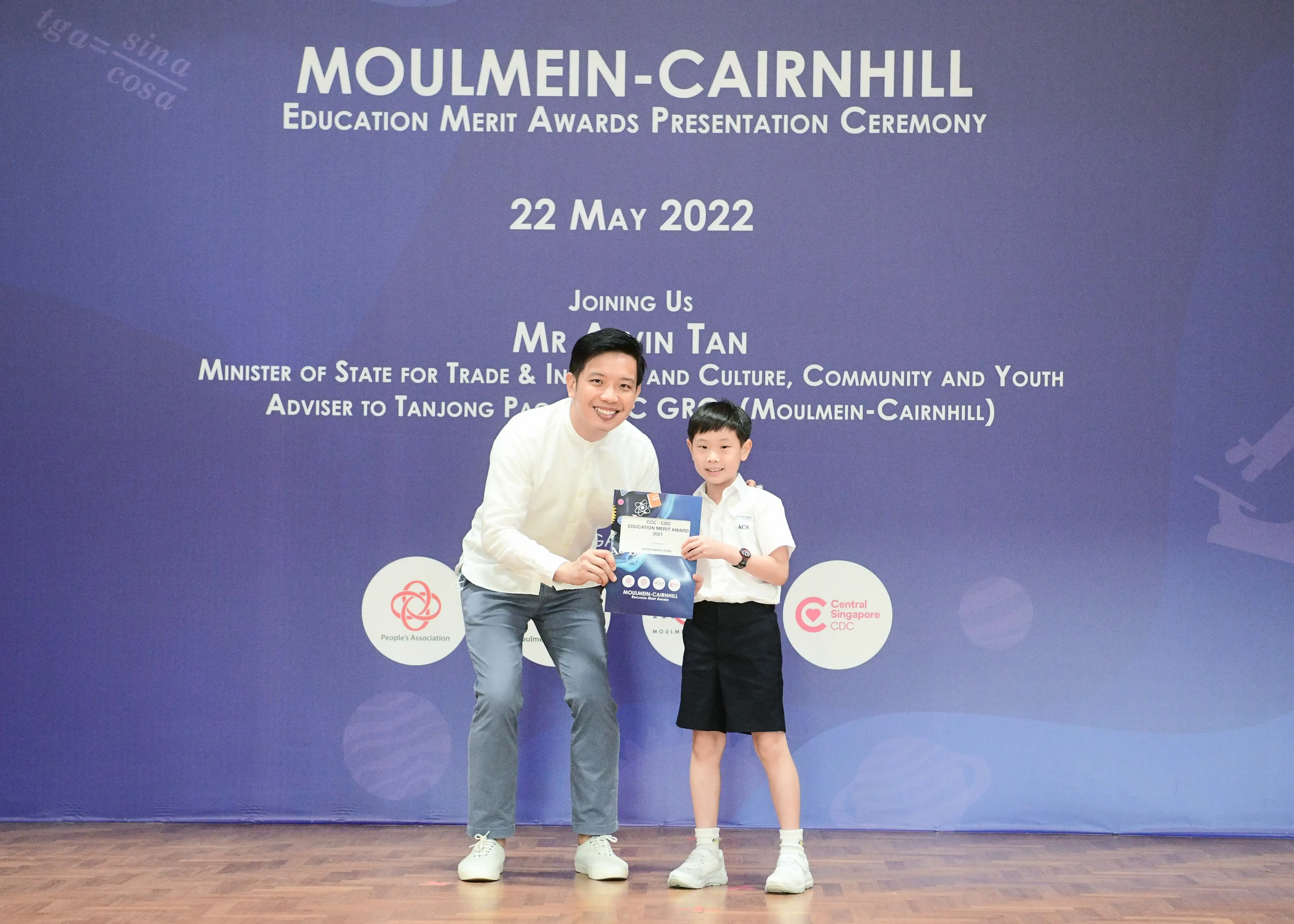 A man and a young boy hold an award certificate on stage at the Moulmein-Cairnhill Education Merit Awards on 22 May 2022.